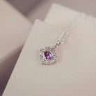 Silver necklace with a purple gemstone pendant on a light pink surface