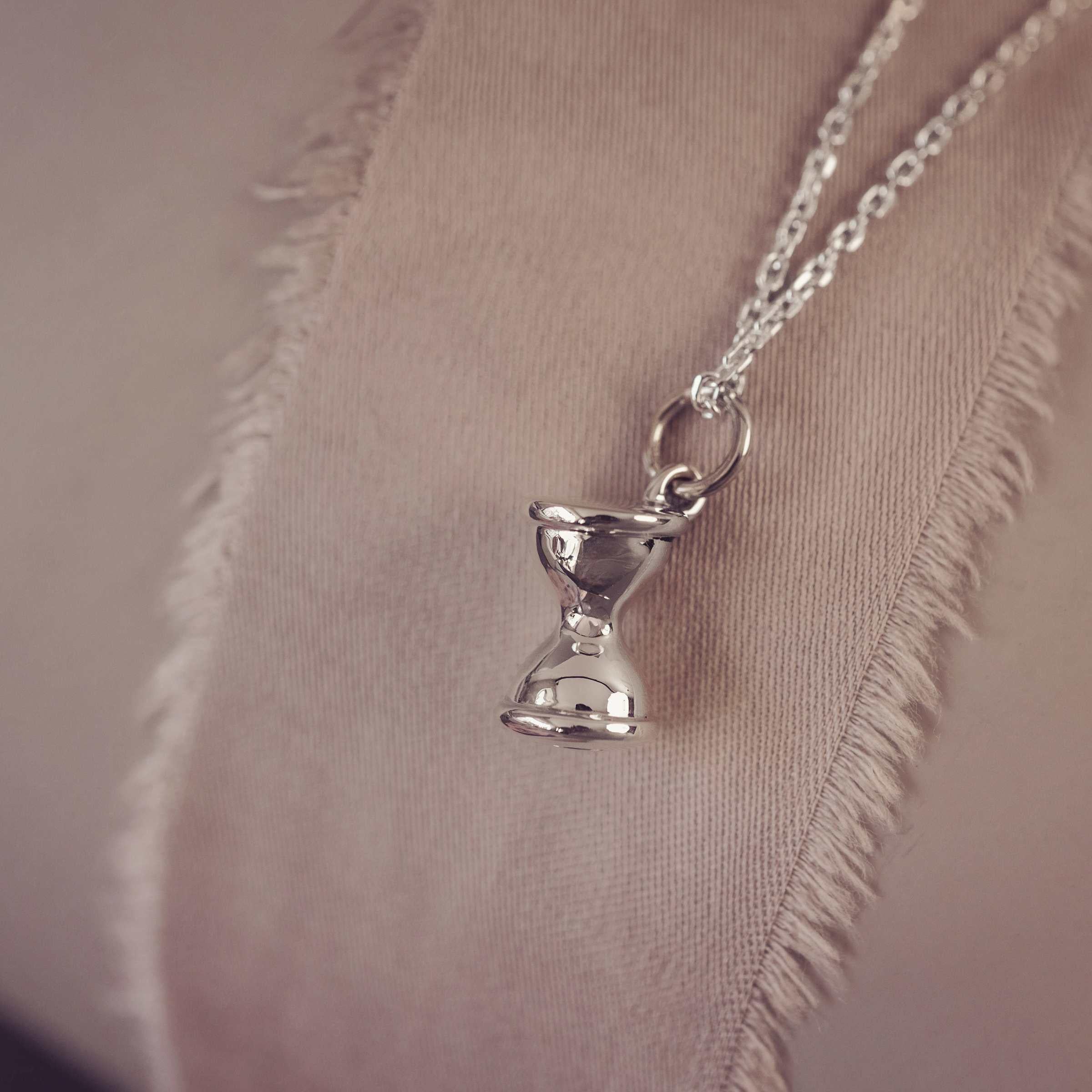 Silver hourglass pendant necklace on a neutral fabric background