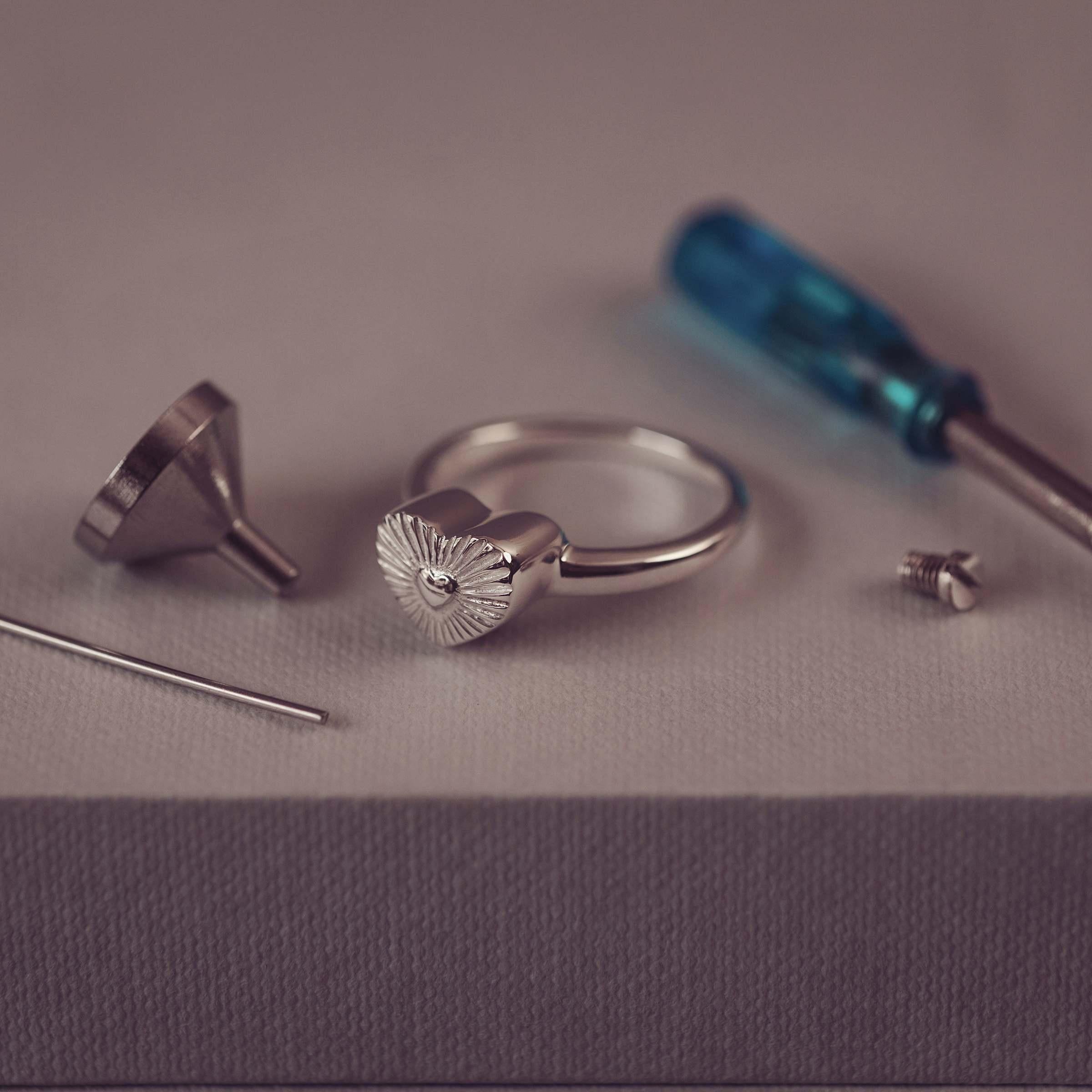 Silver ring with heart design on a gray surface with tools.