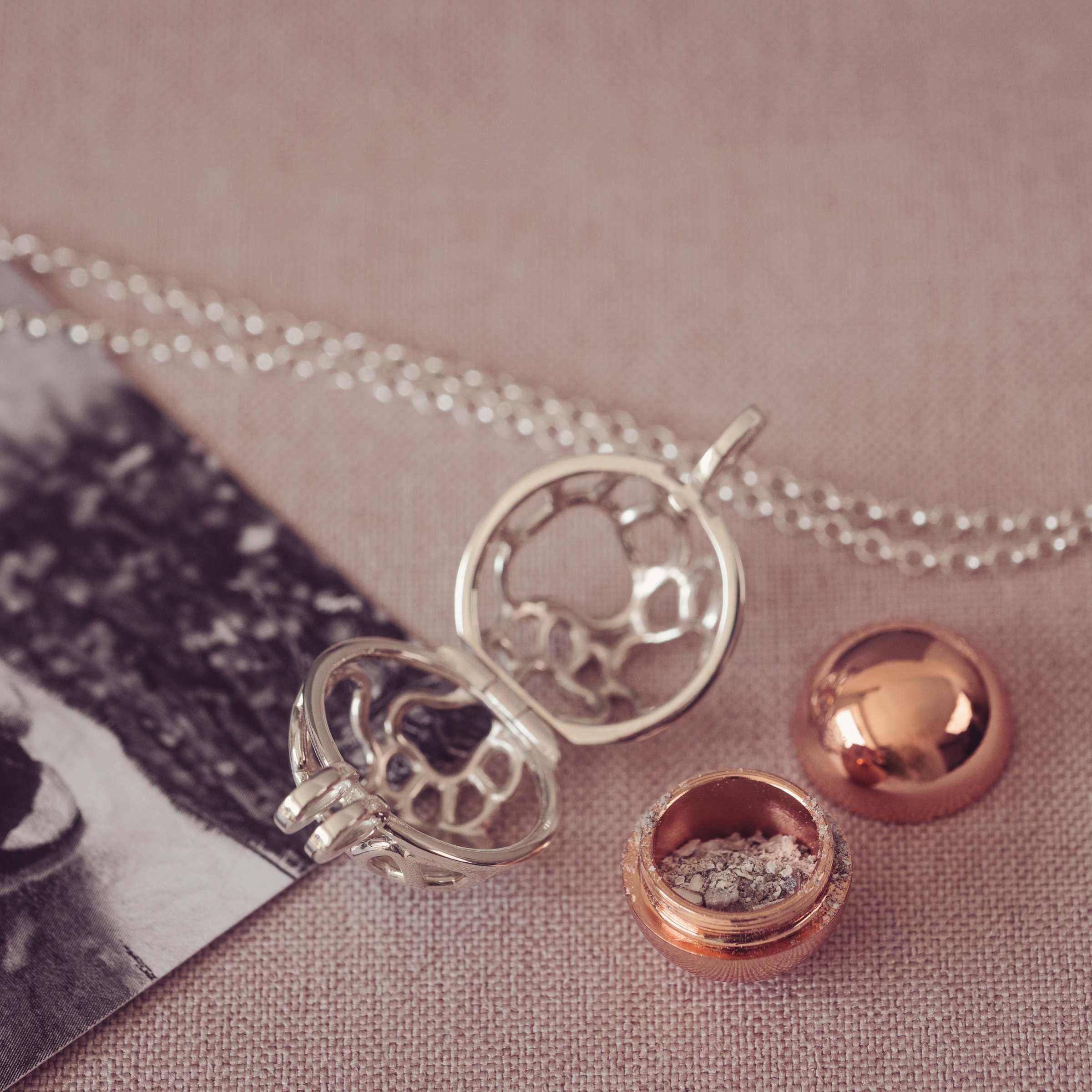 Silver and rose gold necklace with a round locket containing ashes on pink surface.