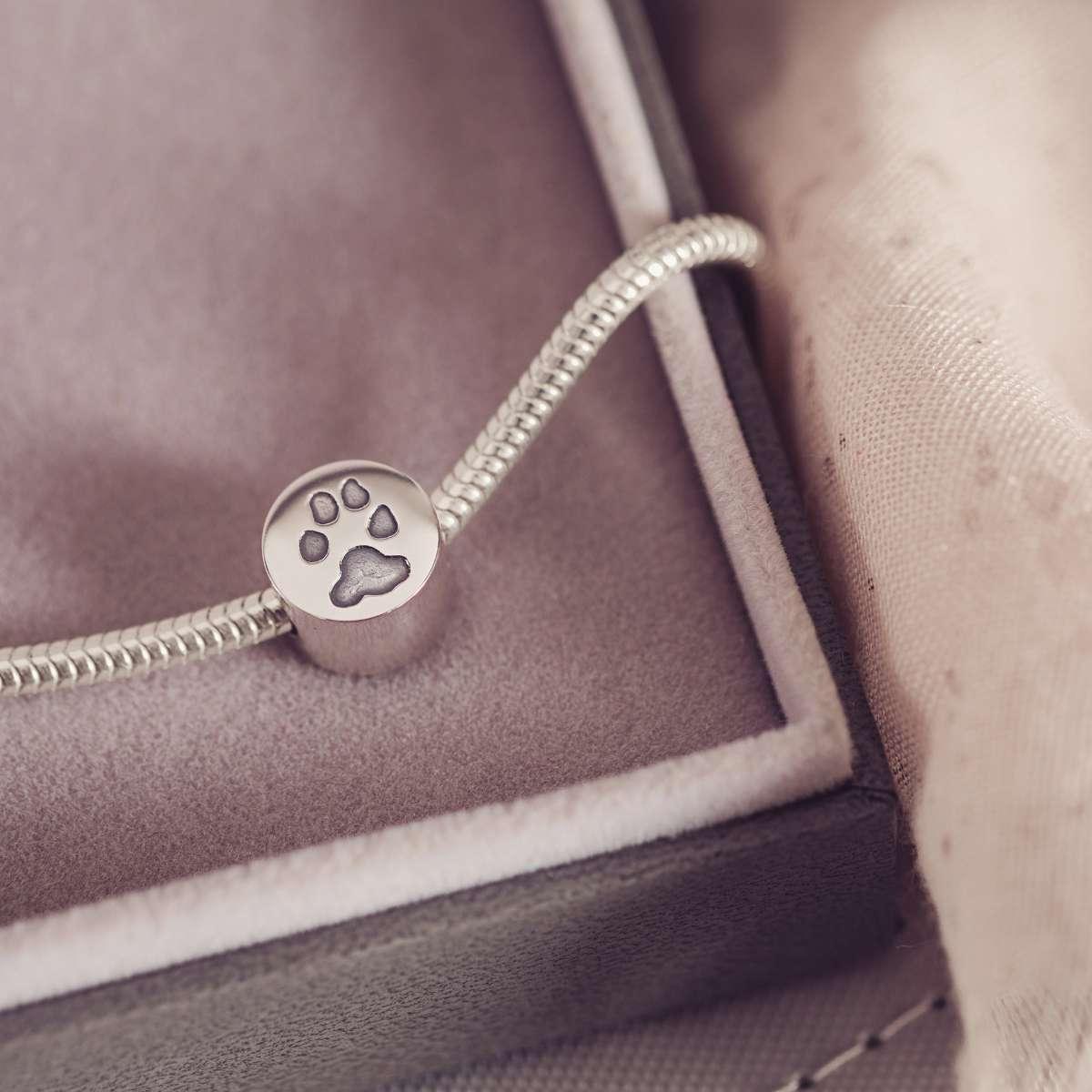 Silver bracelet with a paw print charm on a soft fabric background
