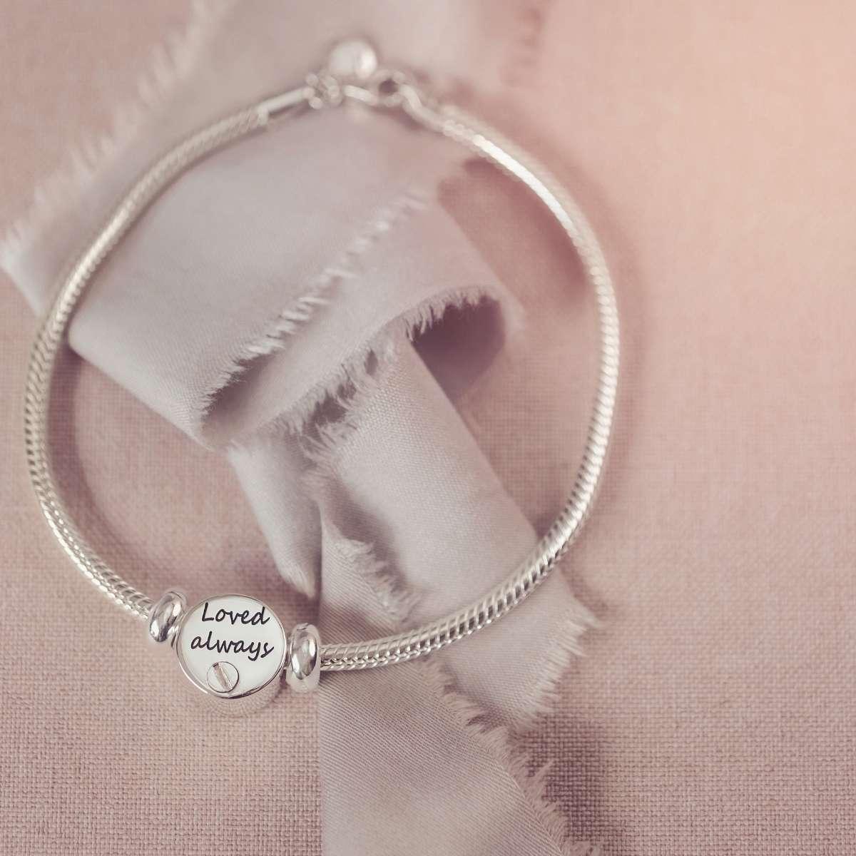 Silver bracelet with a round charm on a soft pink fabric background