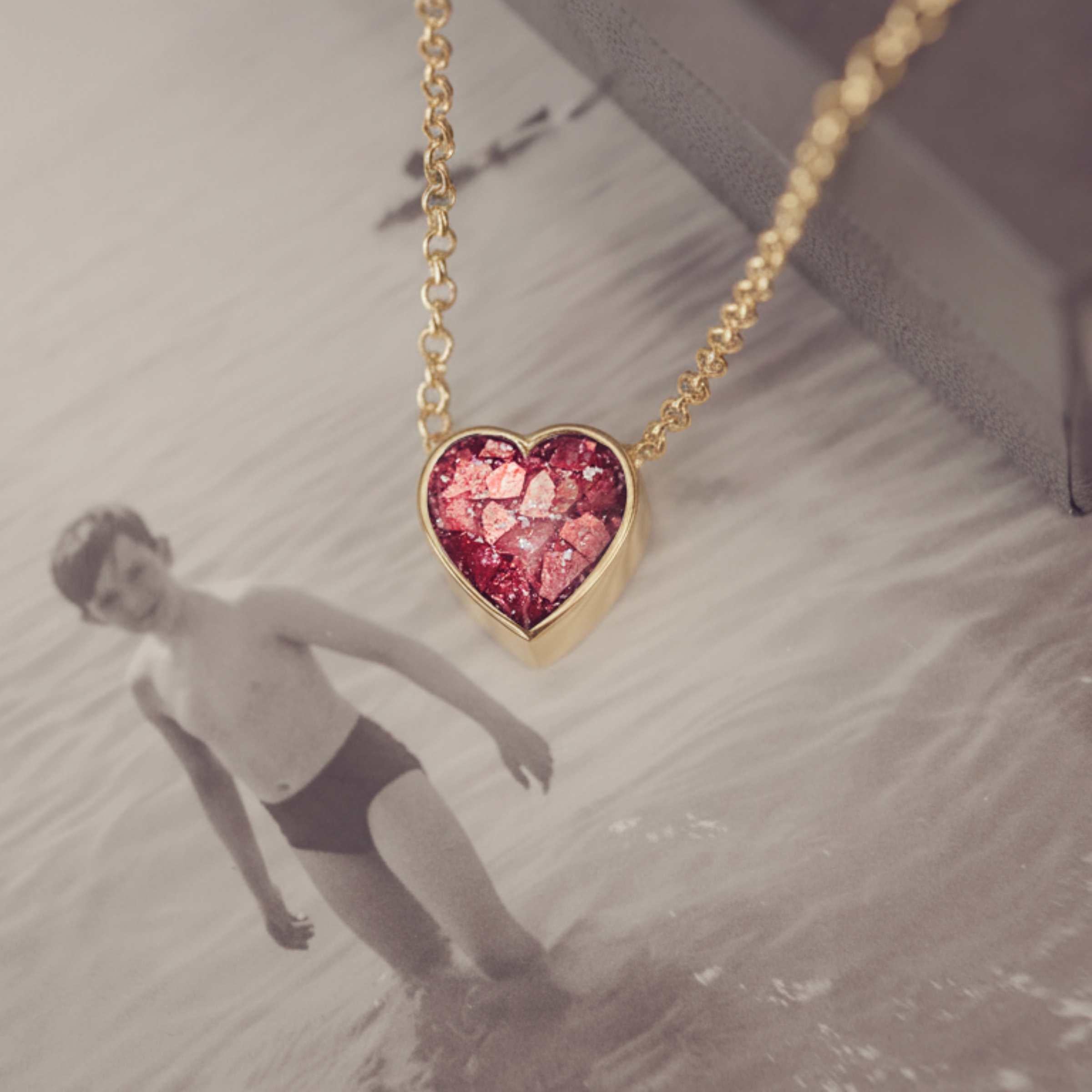Heart-shaped red  necklace on a gold chain with a blurred photograph background 