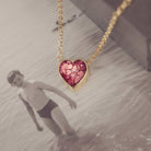 Heart-shaped red  necklace on a gold chain with a blurred photograph background 