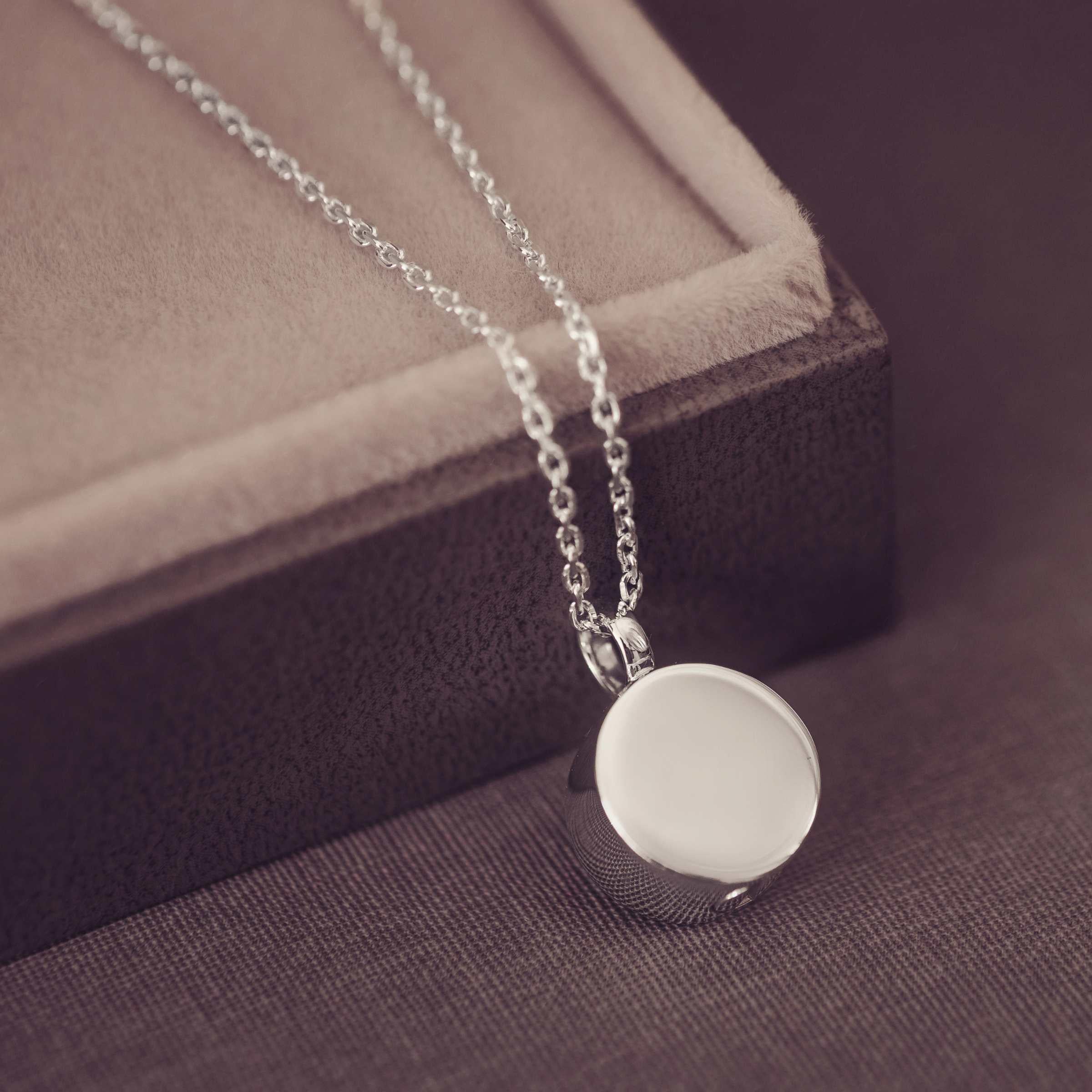 Silver necklace with a round pendant on a textured surface