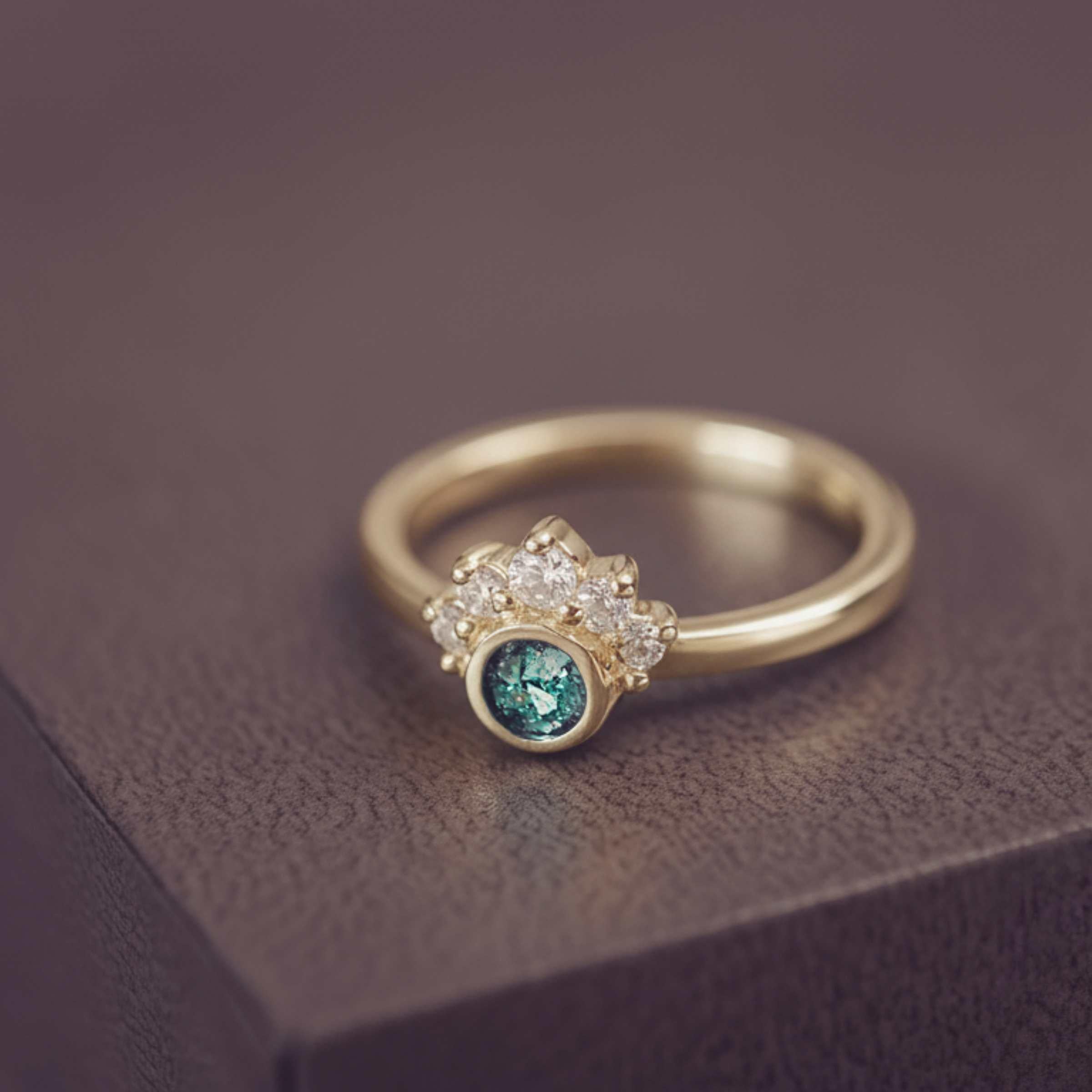 Gold cluster ring with a green  centre and gemstone accents on a dark surface