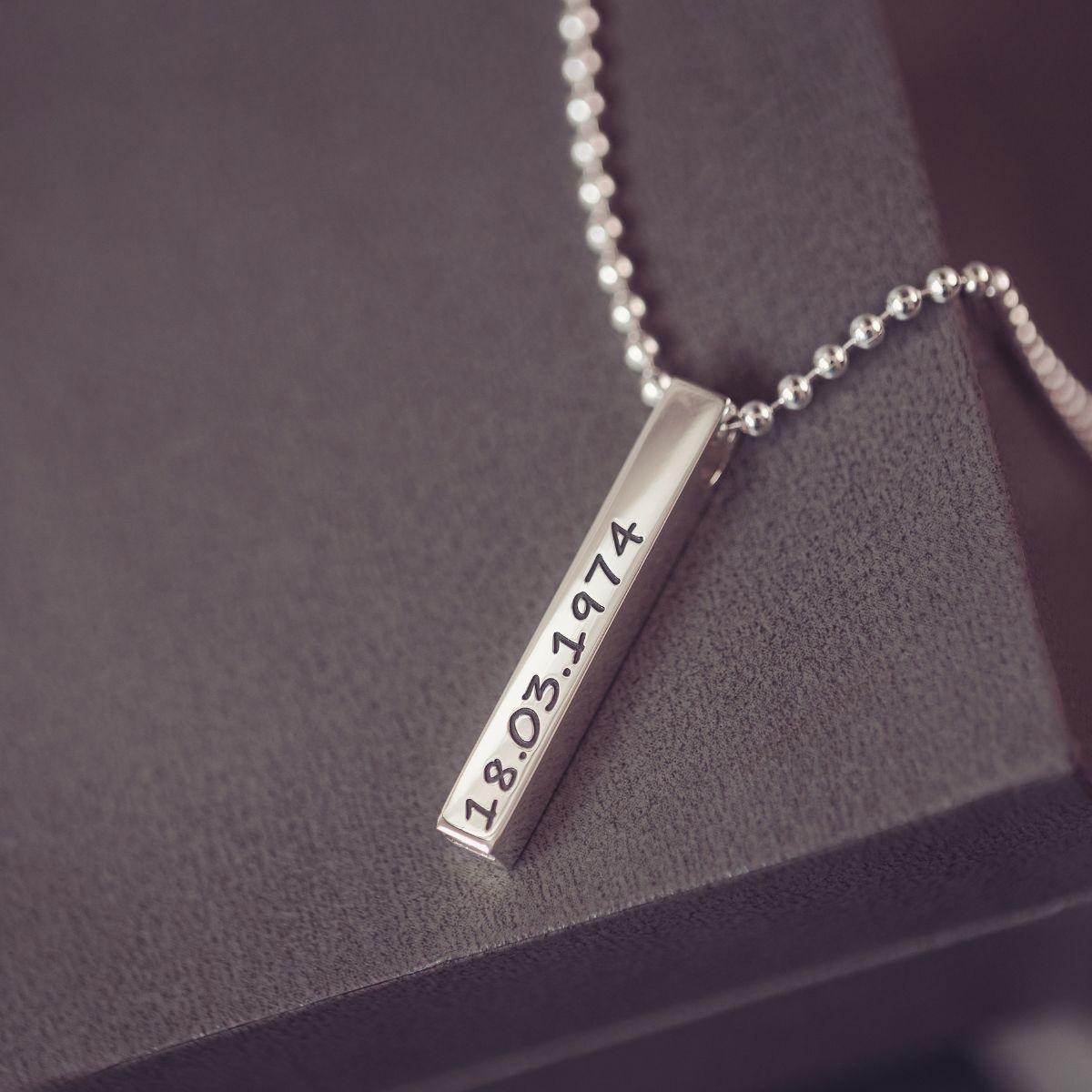 Silver necklace with a bar pendant displaying a date on a dark surface