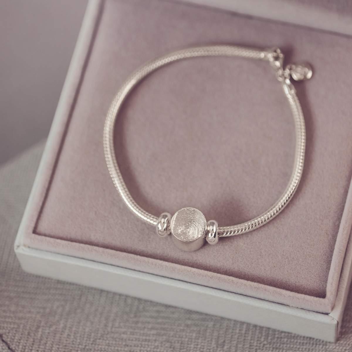 Silver bracelet with a round charm on a pink cushioned surface