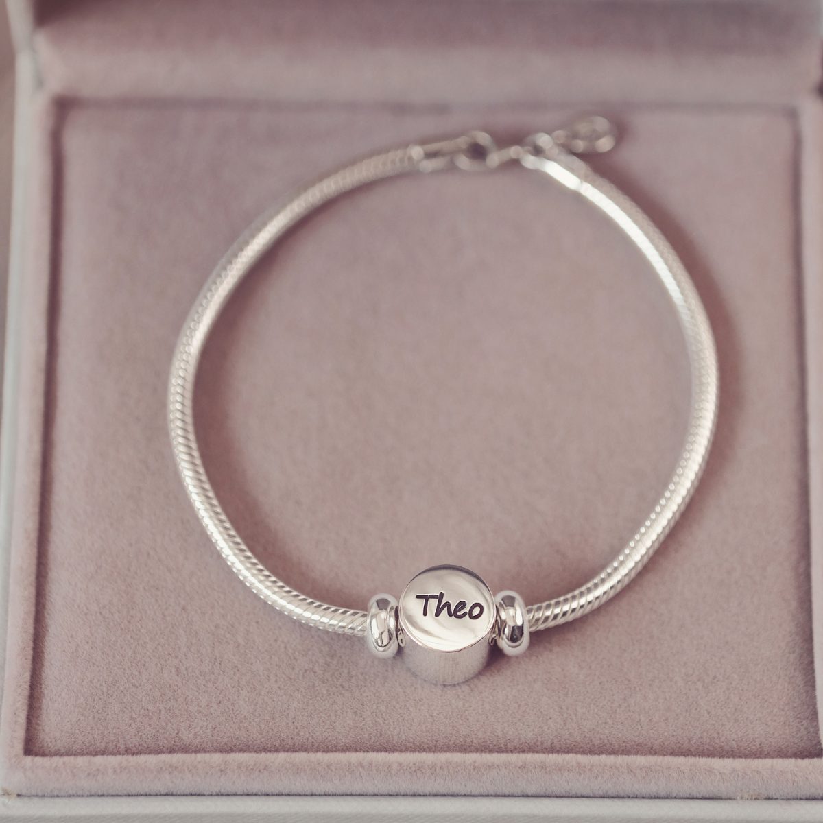 Silver bracelet with a round charm on a pink cushion