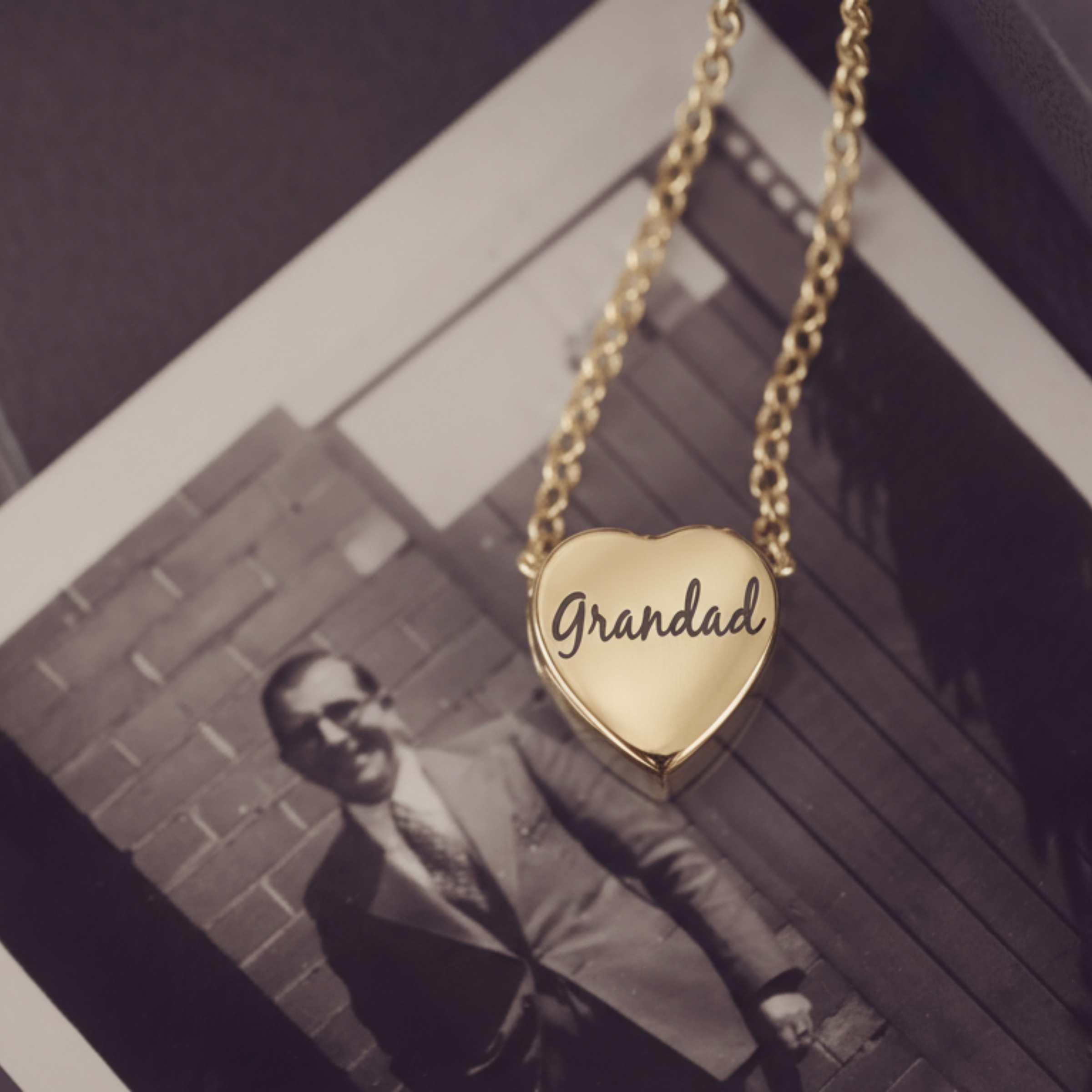 Gold heart-shaped pendant with 'Grandad' engraved, hanging above a black and white photo of a man.