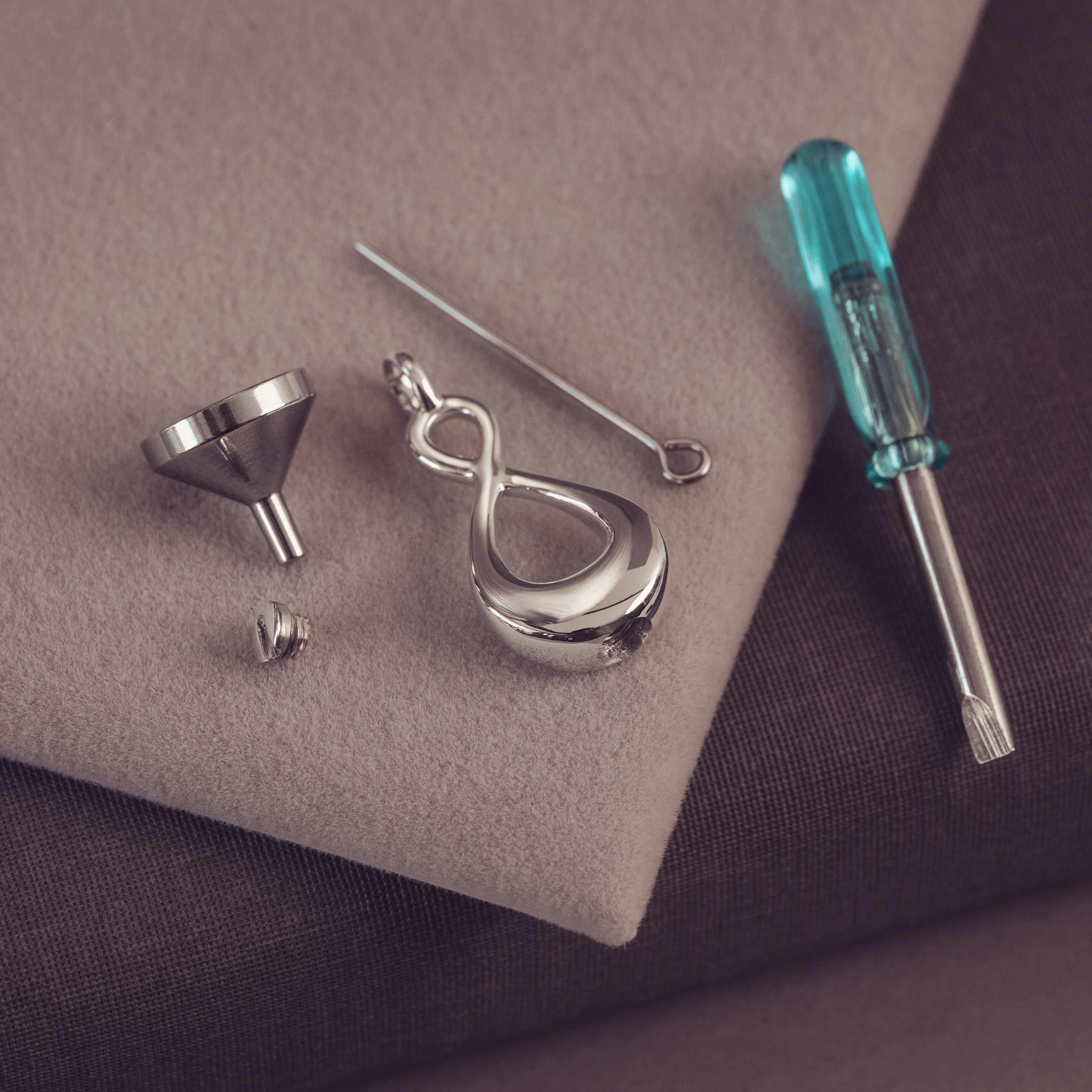 Silver pendant with a jewelery tools including a screwdriver on a textured surface