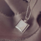 Silver necklace with a square pendant on a soft fabric background