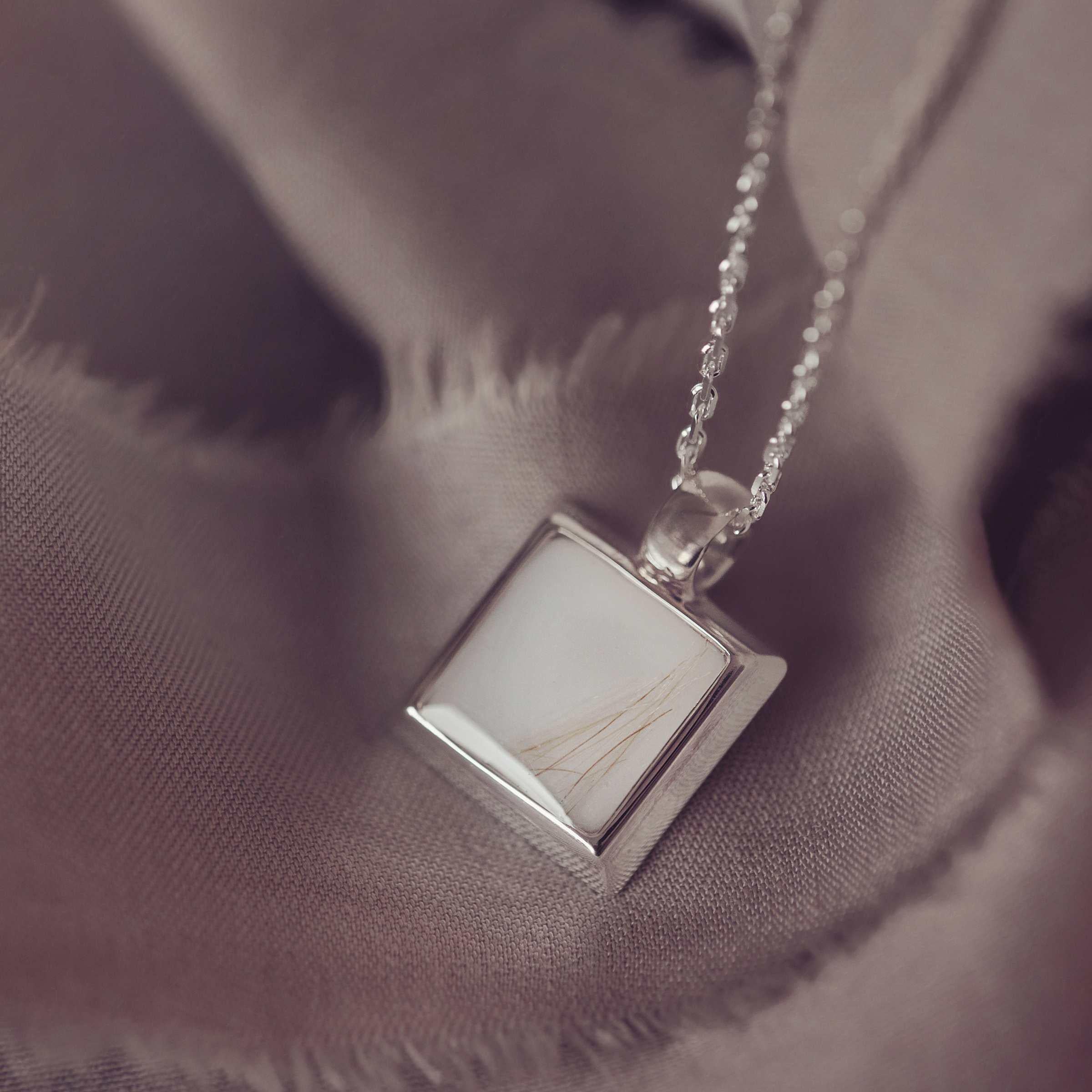 Silver necklace with a square pendant on a soft fabric background
