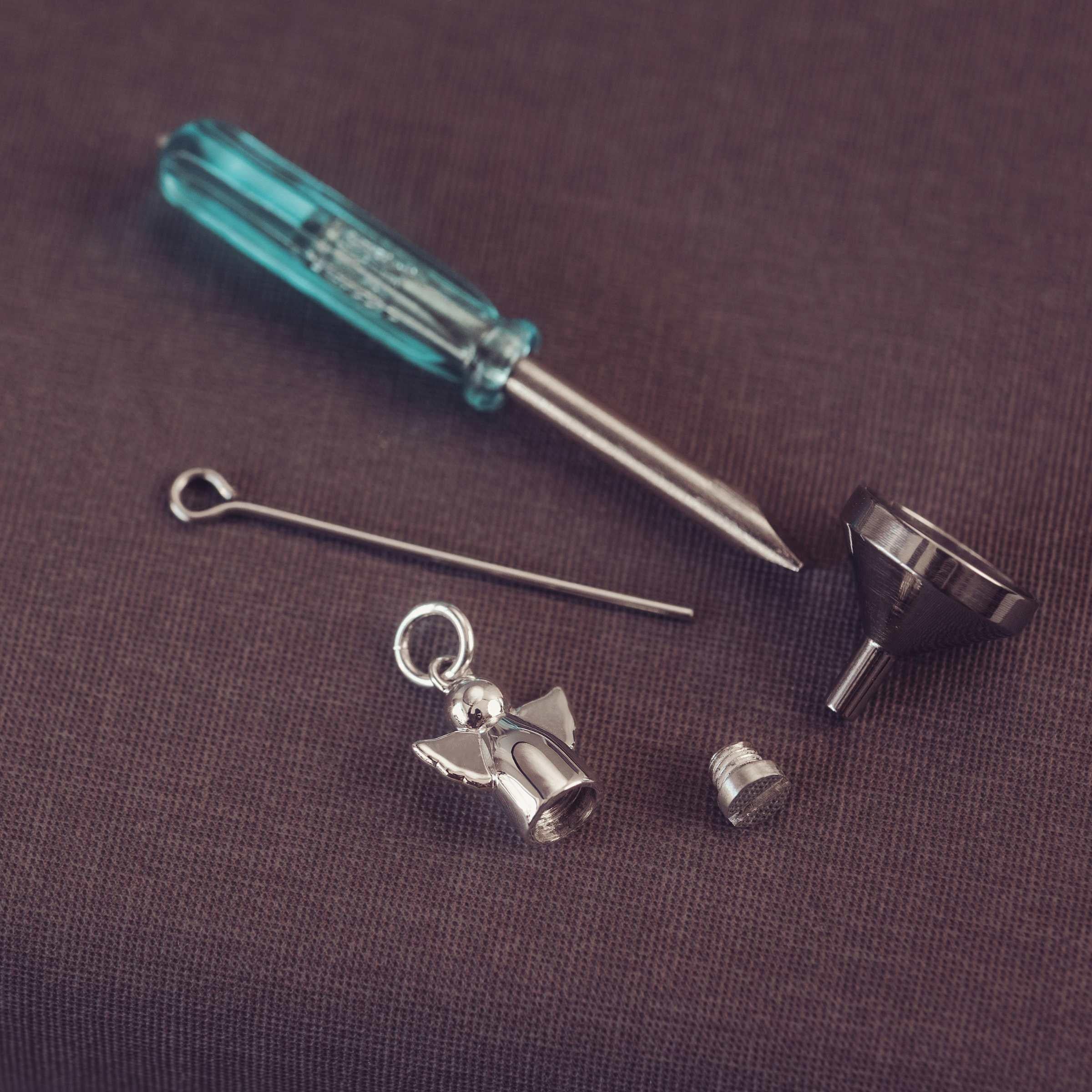 Set of jewellery tools including a screwdriver, needle, angel charm, and funnel on a brown background.