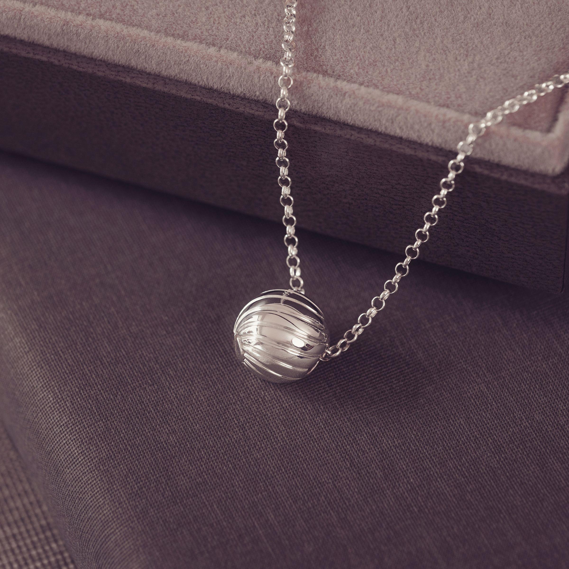 A silver beaded chain necklace with a wave spherical pendant, displayed on a dark textured fabric