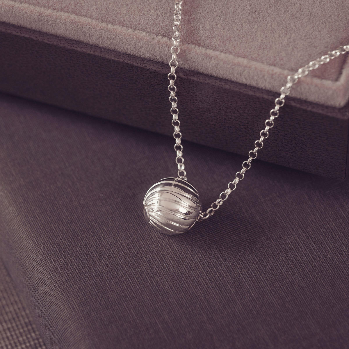 A silver beaded chain necklace with a wave spherical pendant, displayed on a dark textured fabric