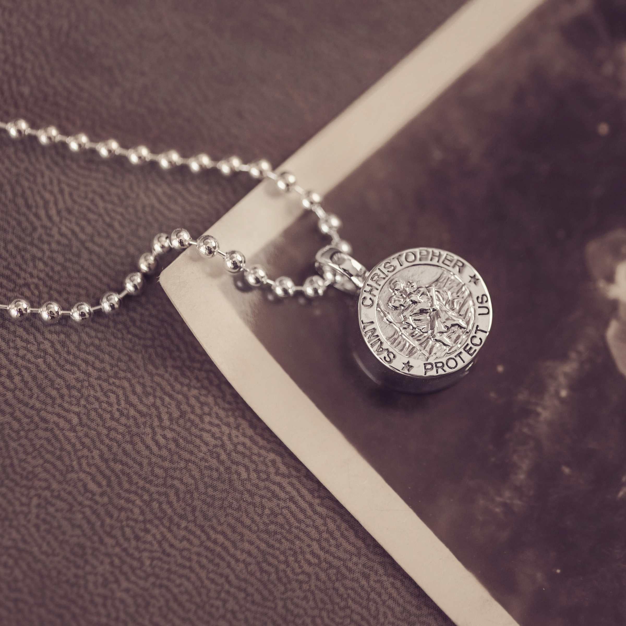 Silver necklace with a St Christopher pendant on a textured surface and vintage photograph