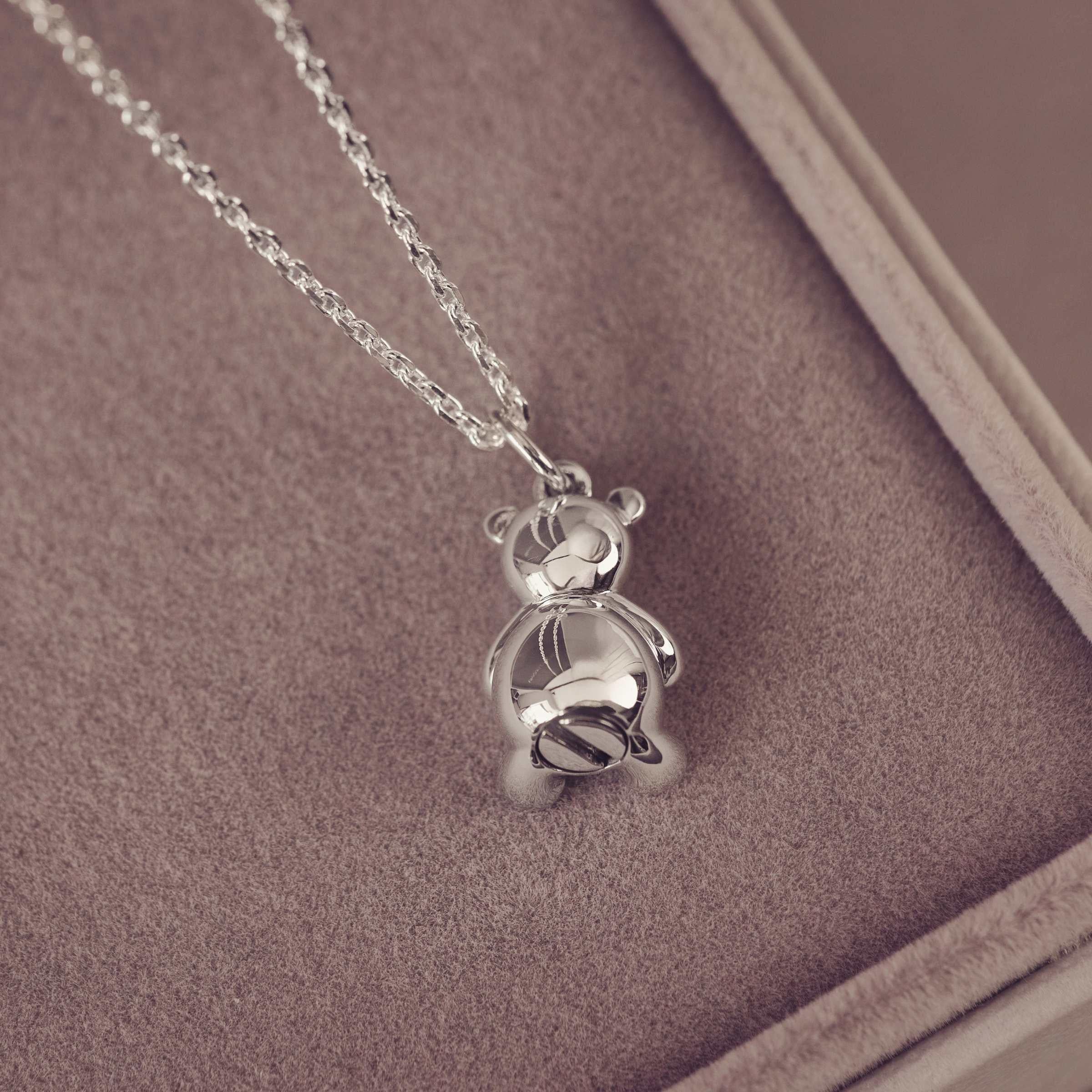Silver teddy bear pendant on a chain against a brown background