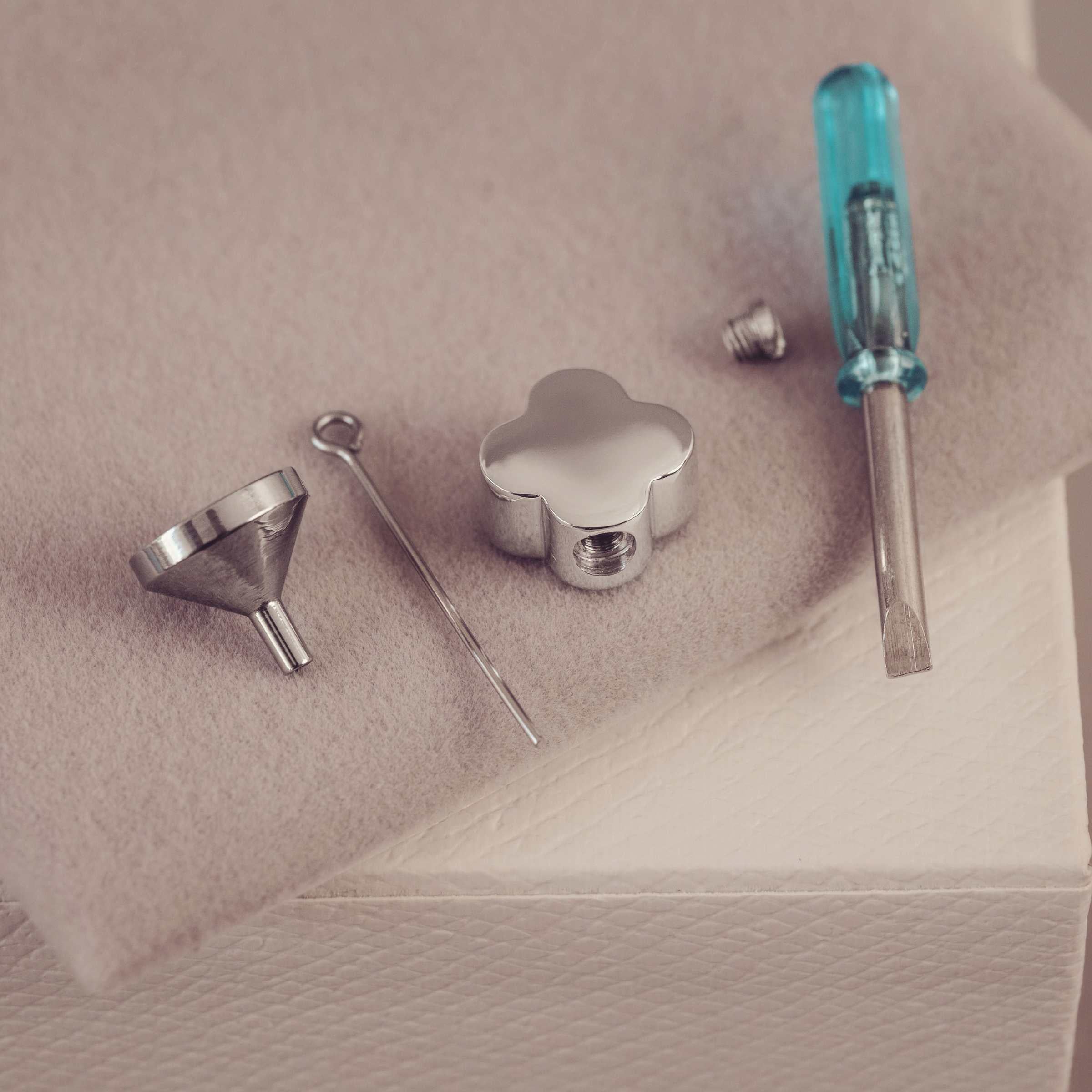 Set of jewellery tools including a funnel, screwdriver and pendant on  beige surface.