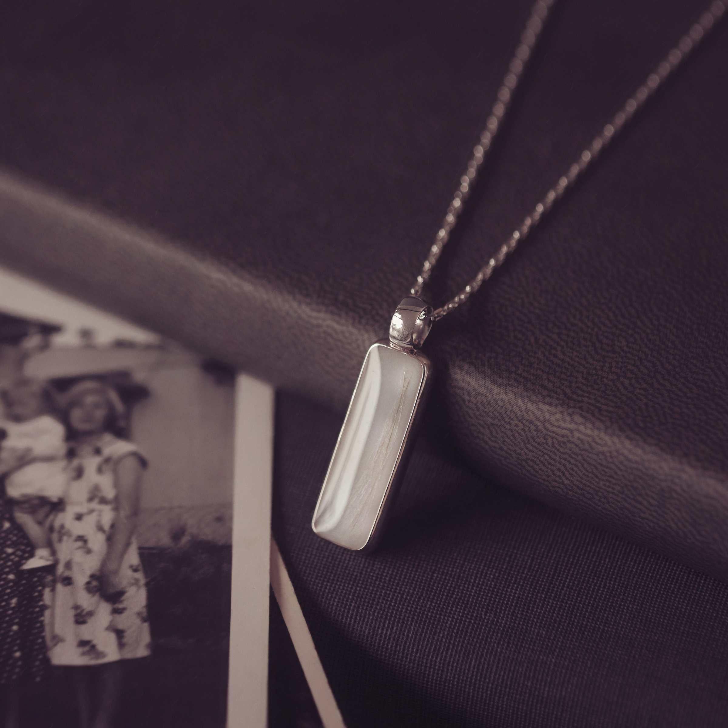 Silver pendant necklace on a dark fabric background with an old photograph of a woman in a floral dress.