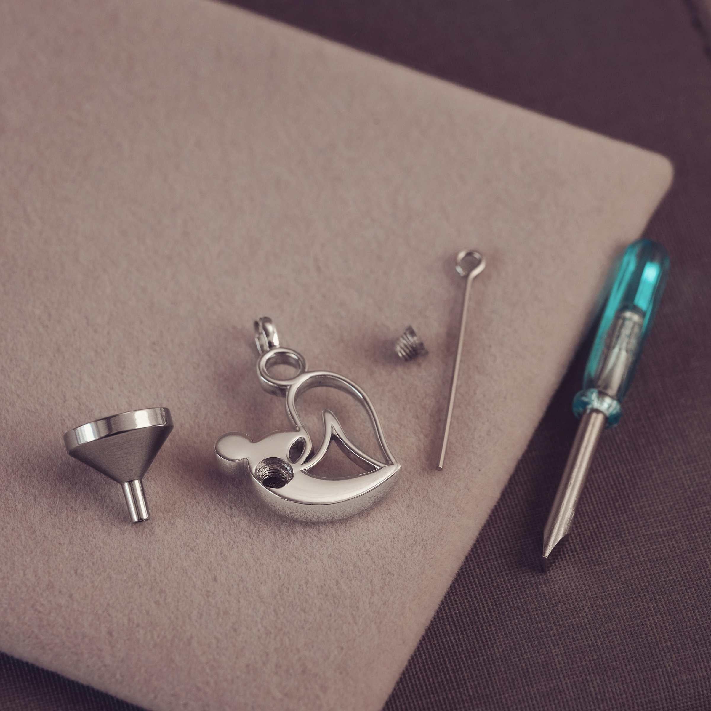 Silver pendant, funnel and screwdriver on a brown surface