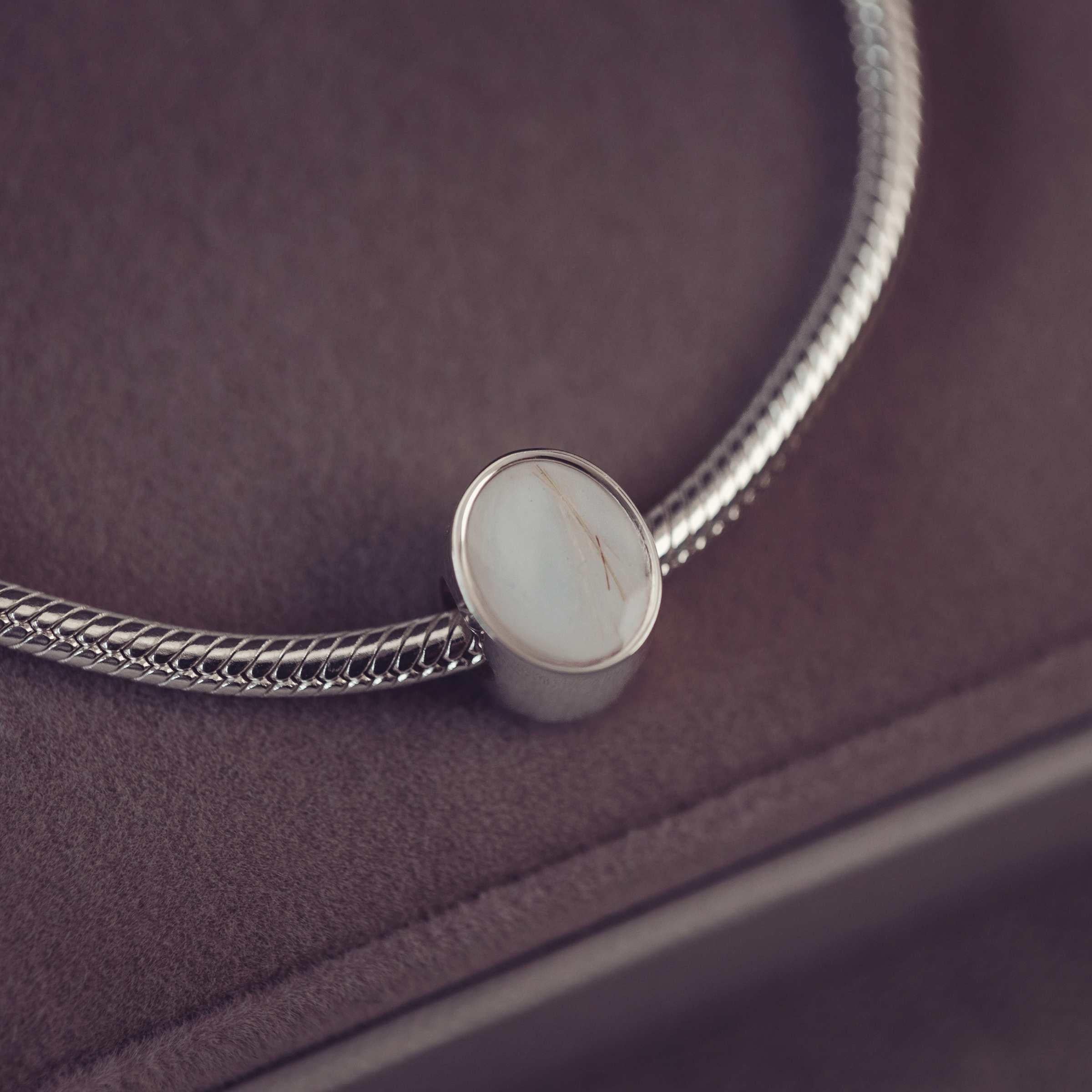 Silver bracelet with an oval charm on a dark surface