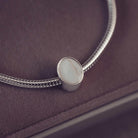 Silver bracelet with an oval charm on a dark surface