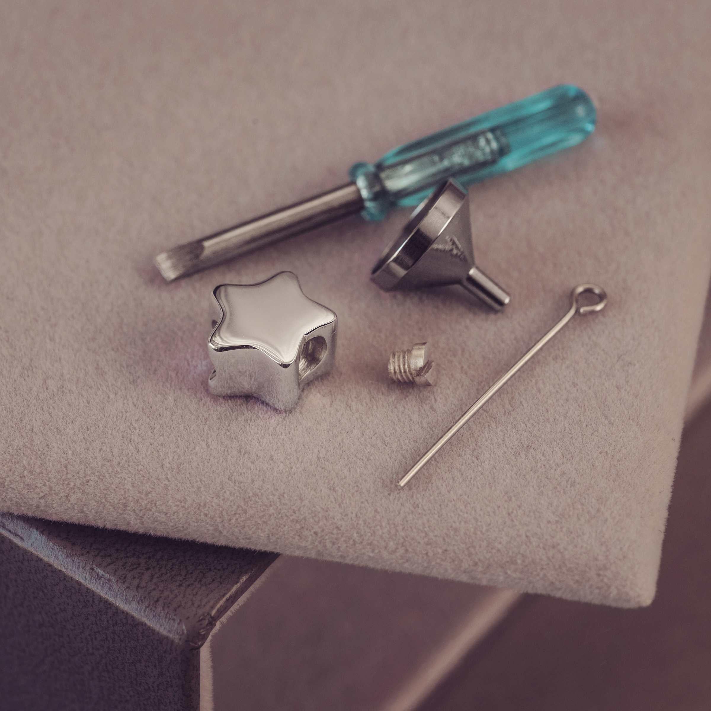 Set of jewelry-making tools including a star-shaped component, screwdriver, and needle on a textured surface.