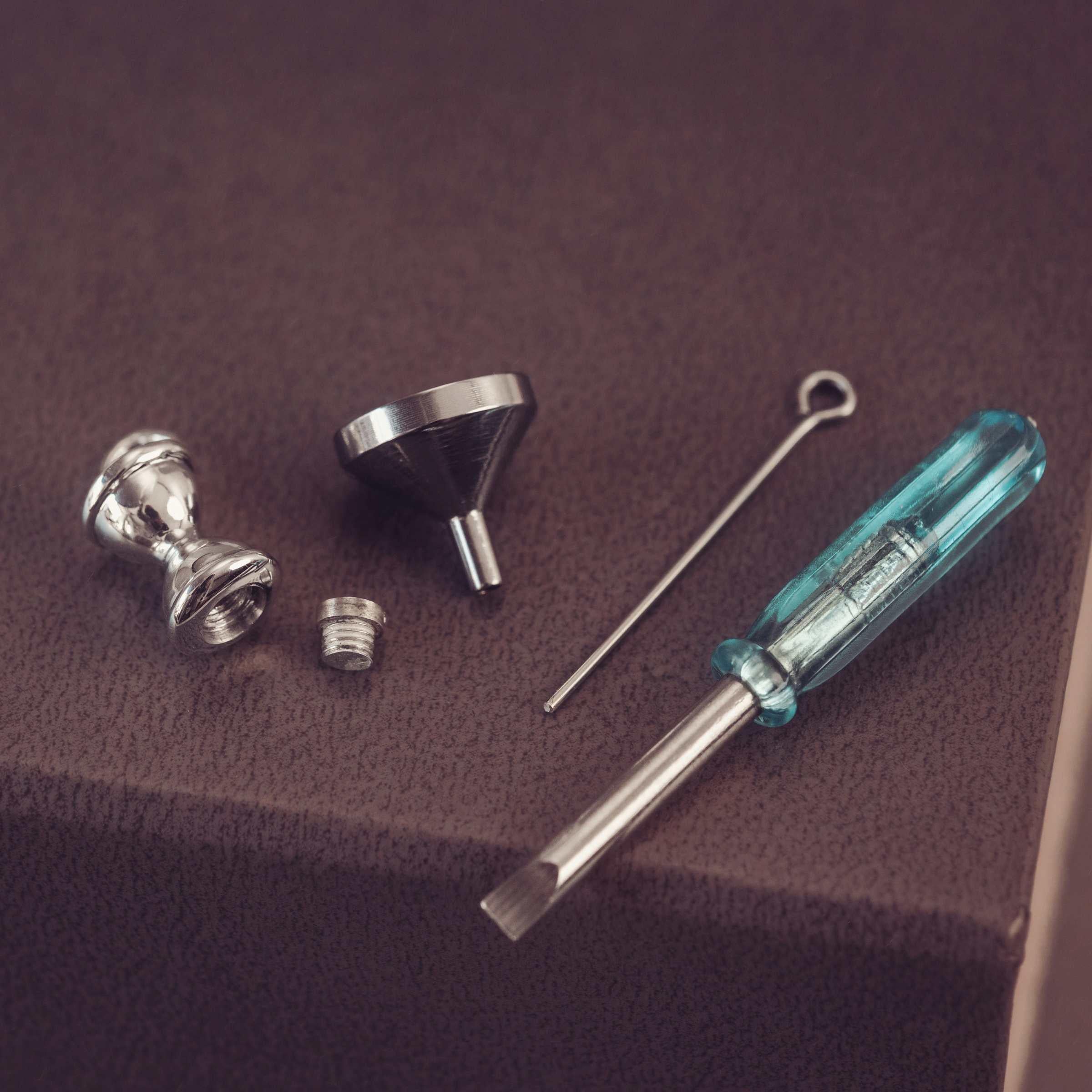 Set of metal tools including a screwdriver, funnel, and hourglass pendant on a brown surface.