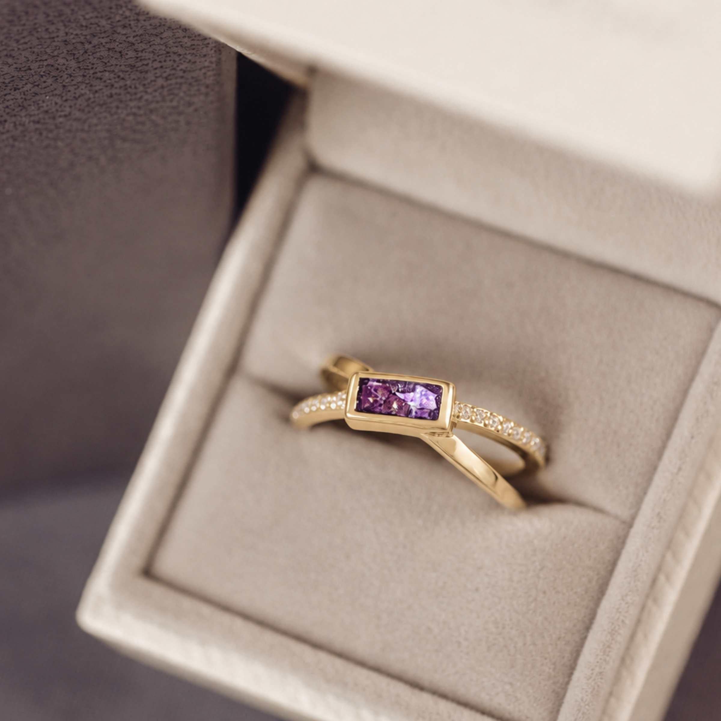 gold criss cross ring with a purple rectangle ash stone and gemstones in a jewellery box