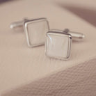 Silver square cufflinks on a textured beige surface