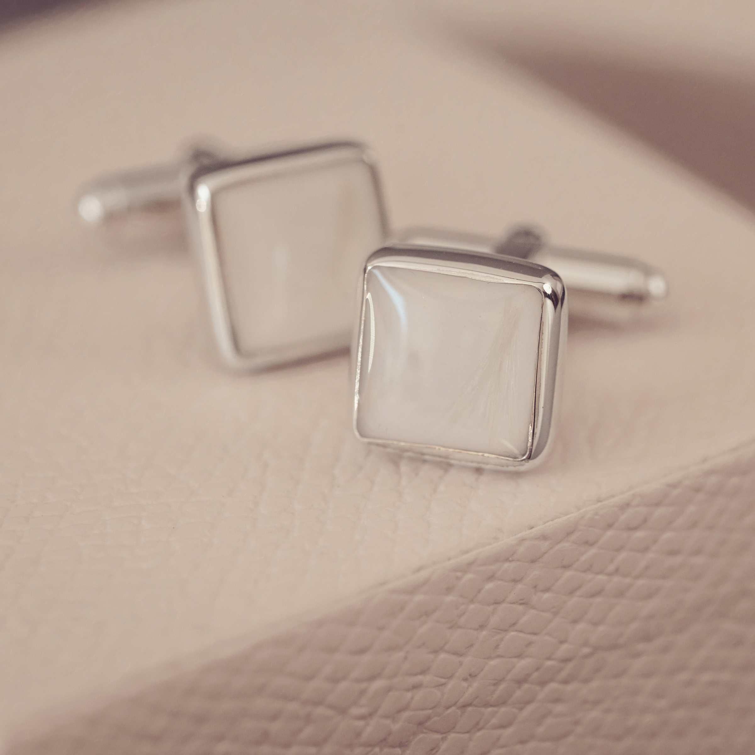 Silver square cufflinks on a textured beige surface