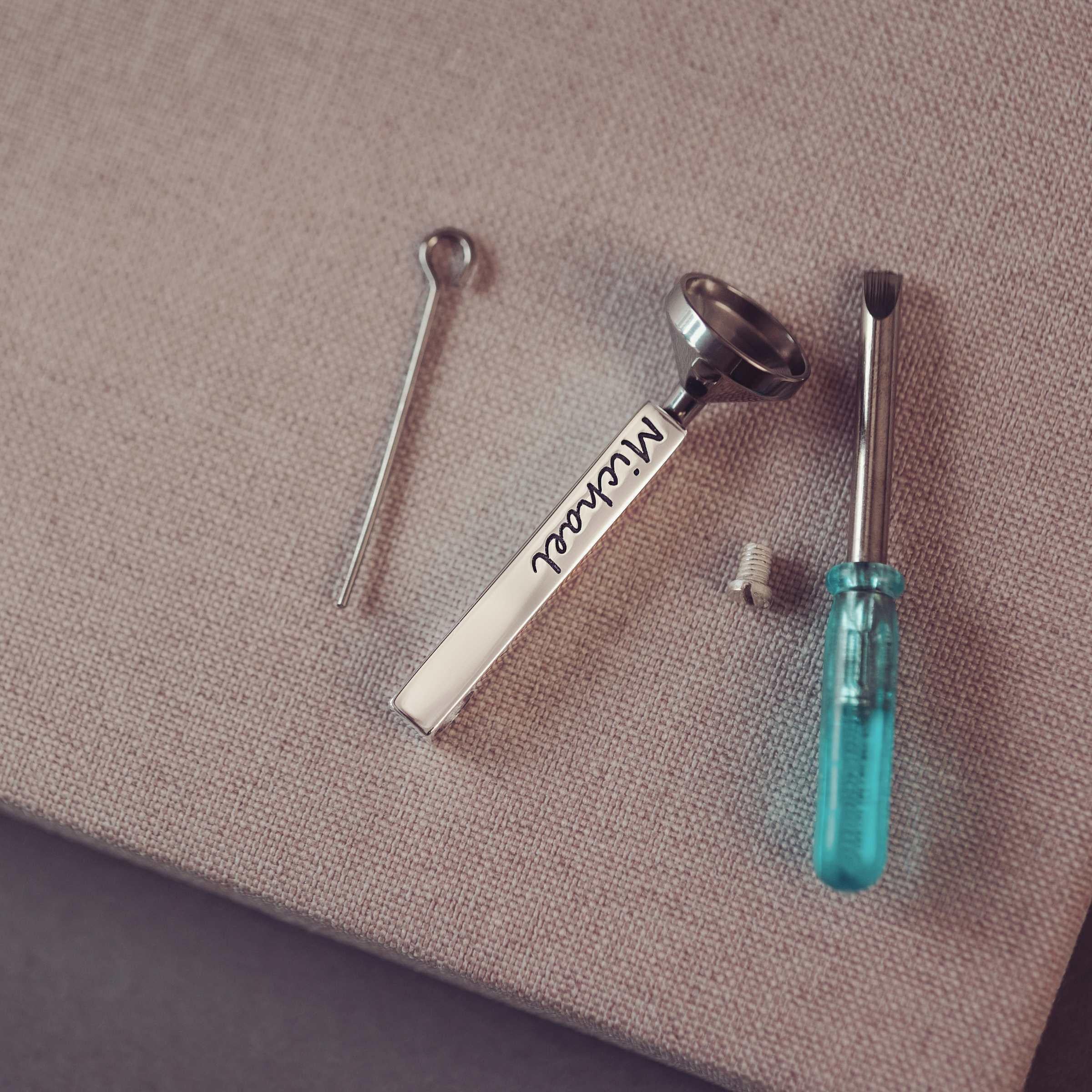 Set of small tools including a screwdriver, funnel and bar pendant on a textured surface.