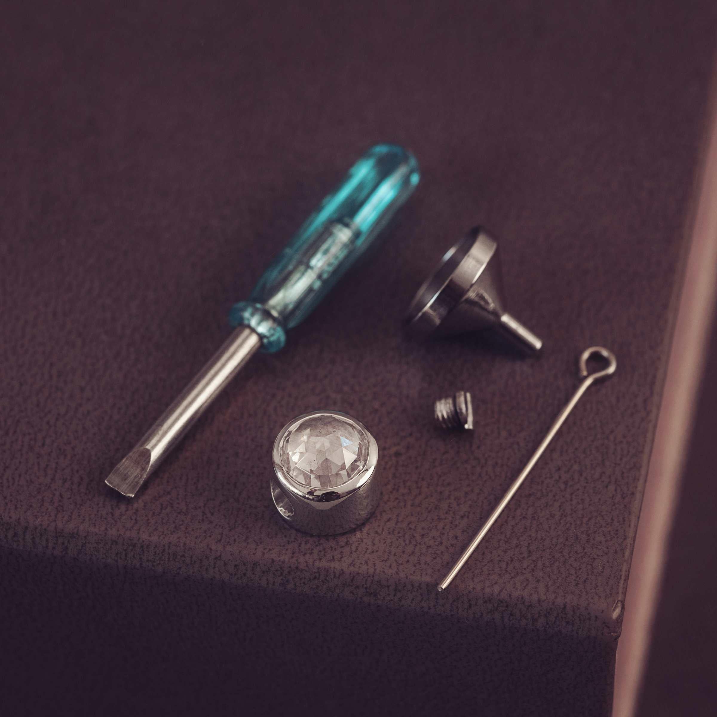 Set of tools including a screwdriver, funnel, and pins on a dark surface.