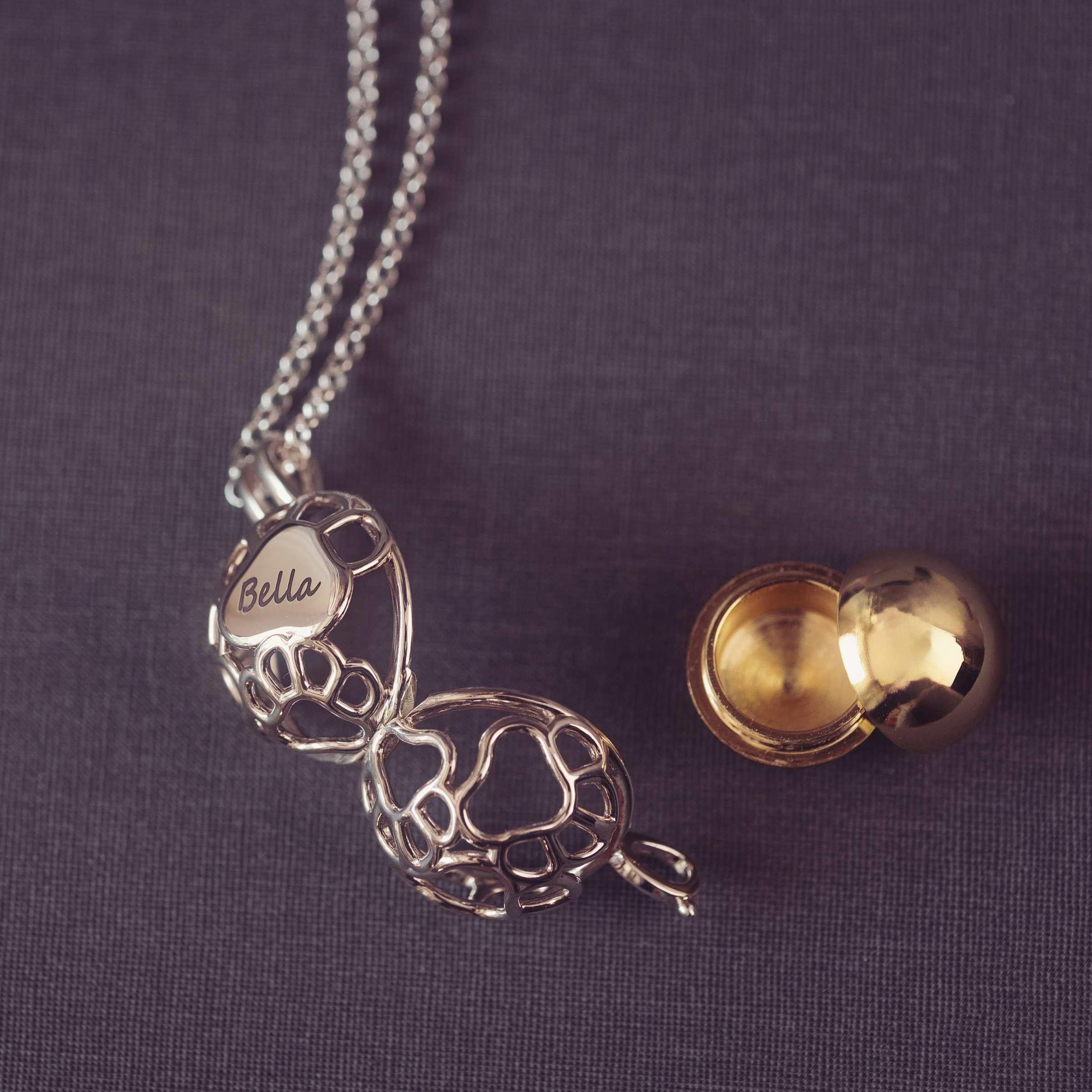 Silver necklace with a paw shaped pendant and yellow locket on a purple fabric background