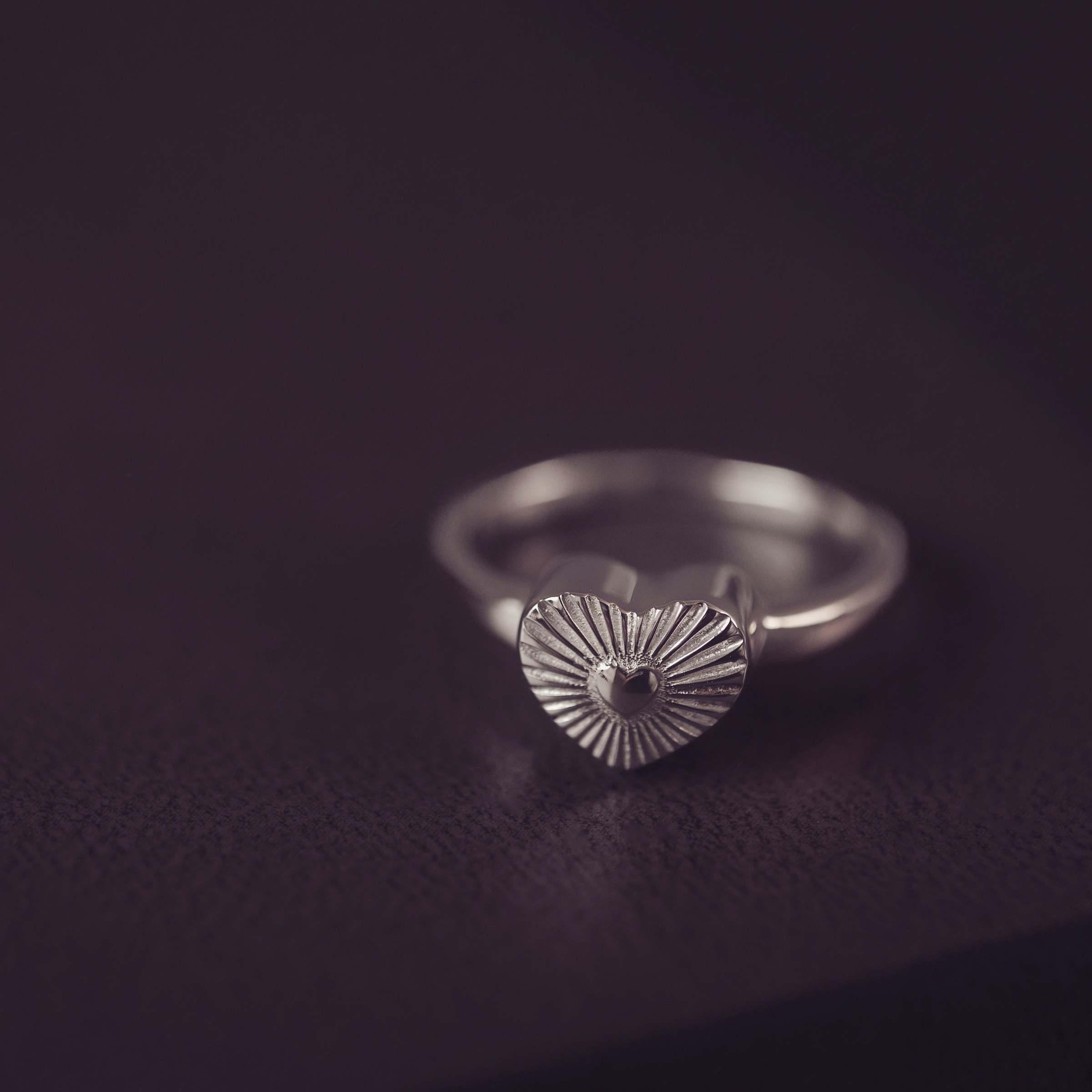 Silver ring with a textured heart-shaped design on a dark background