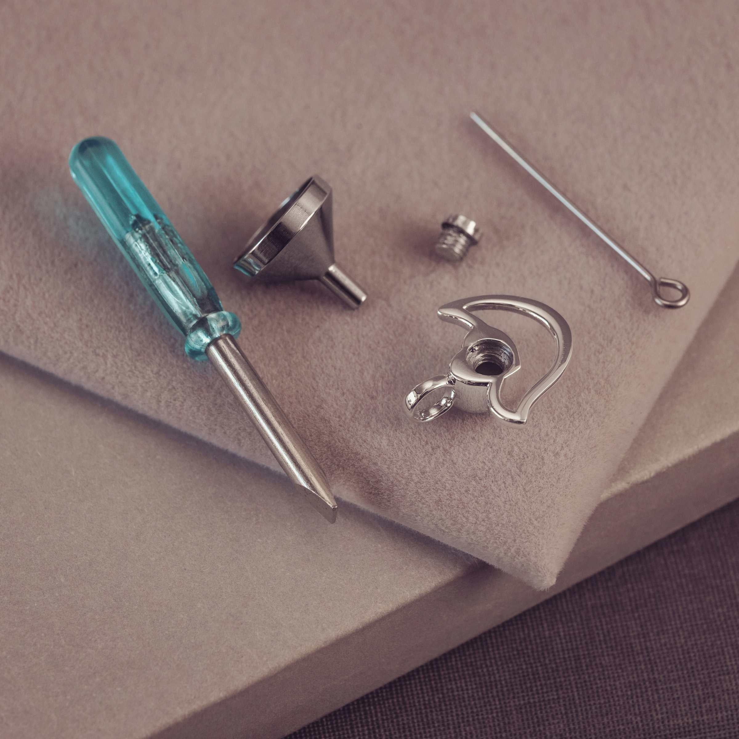 Jewellery tools including a screwdriver and metal components on a beige surface.
