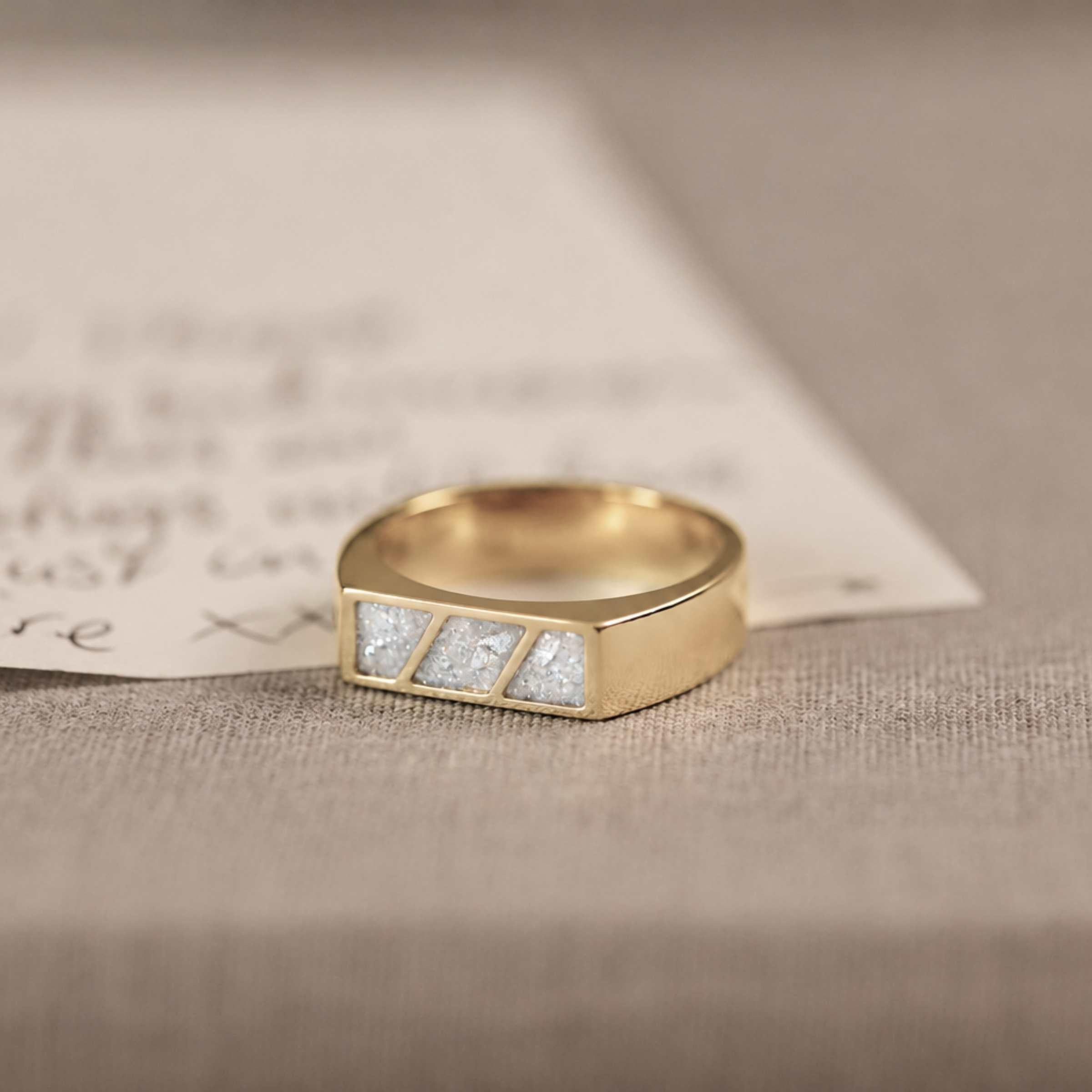 A gold ring with 3 sections of white resin across the top. Sitting on a hand written letter and textured background