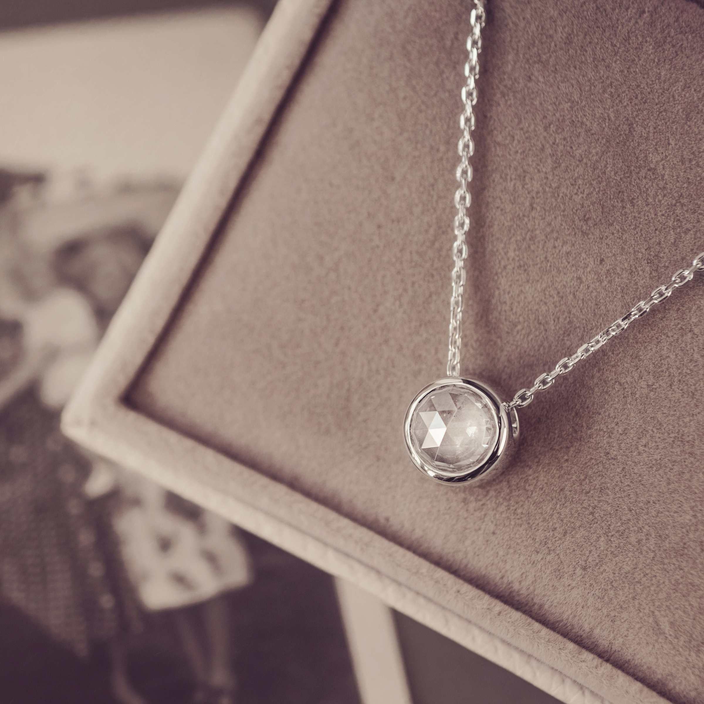 Silver necklace with round gemstone in a jewellery box next to a black and white image.