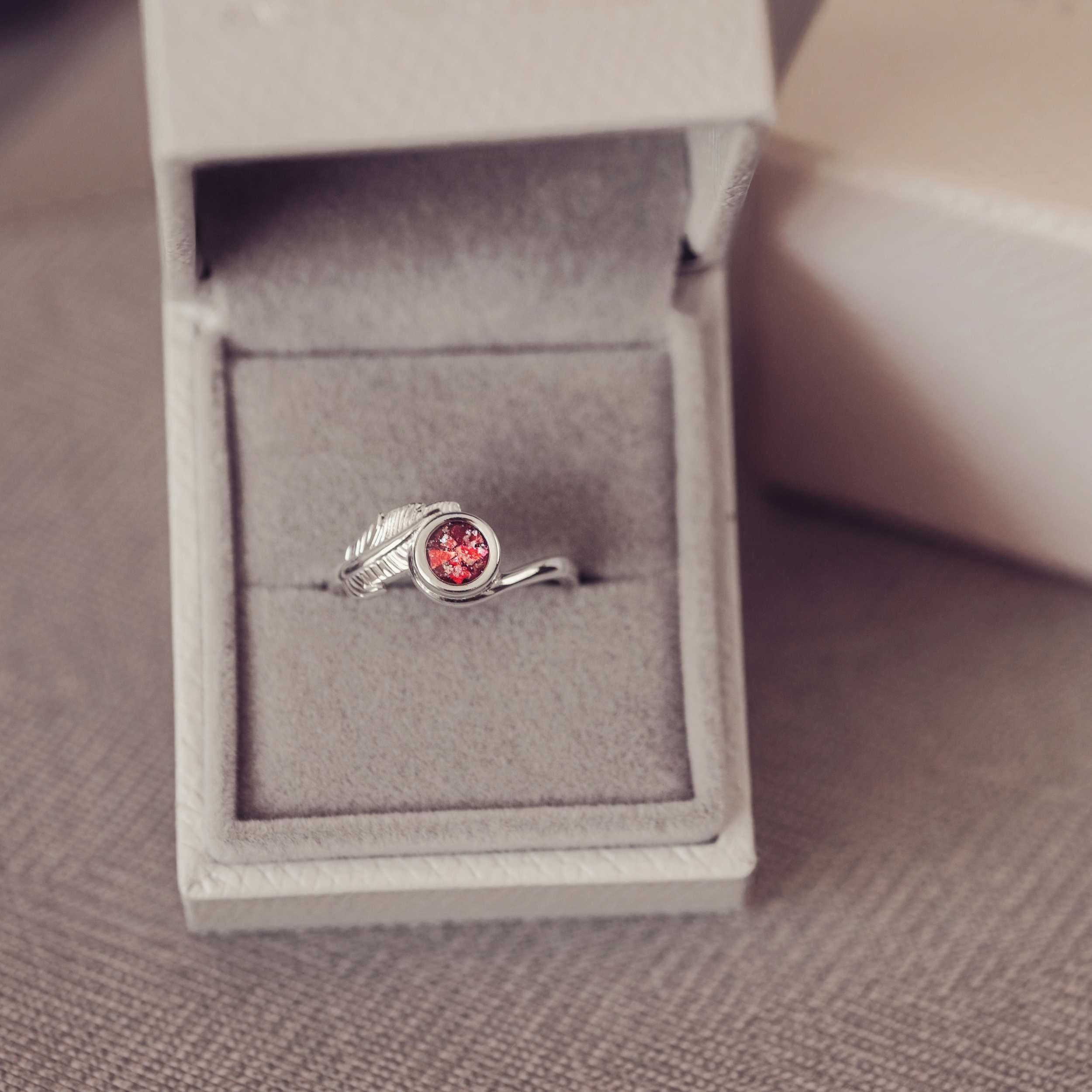 A silver red ash filled feather ring in a jewellery box