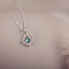 Silver heart-shaped pendant with a green gemstone on a soft background
