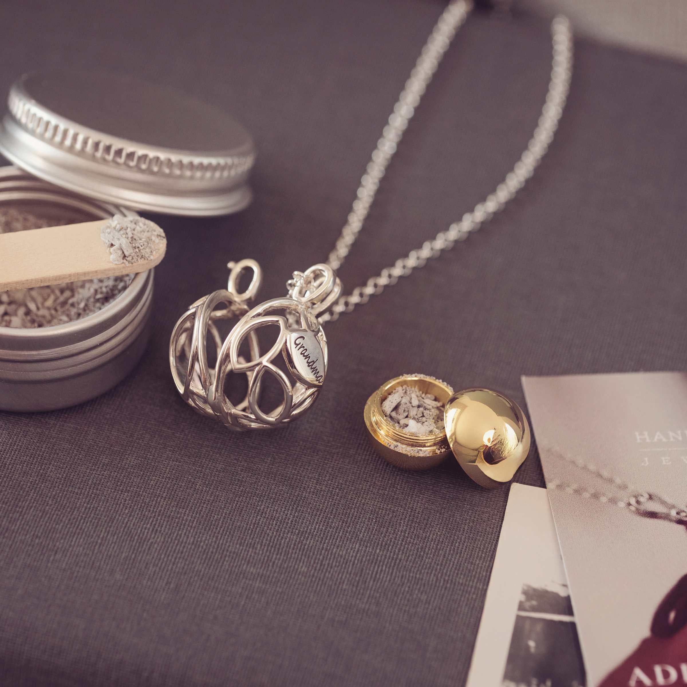 Silver and gold necklaces on a textured surface with small containers and photos.