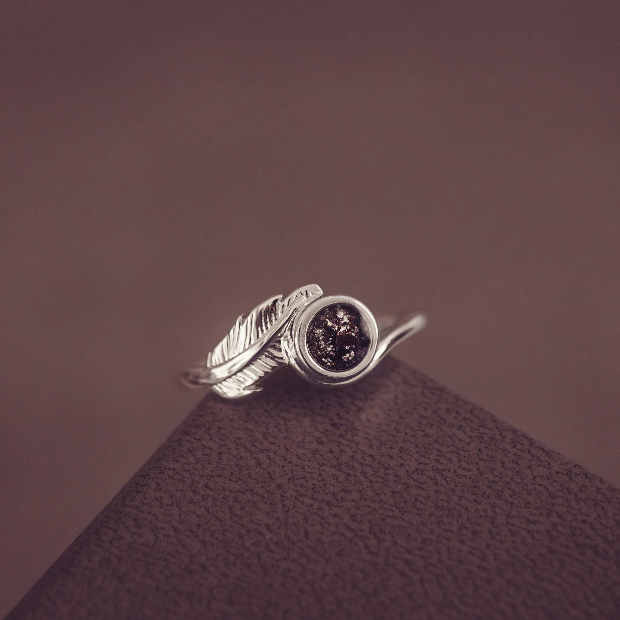 A silver black ash filled feather ring on dark textured background