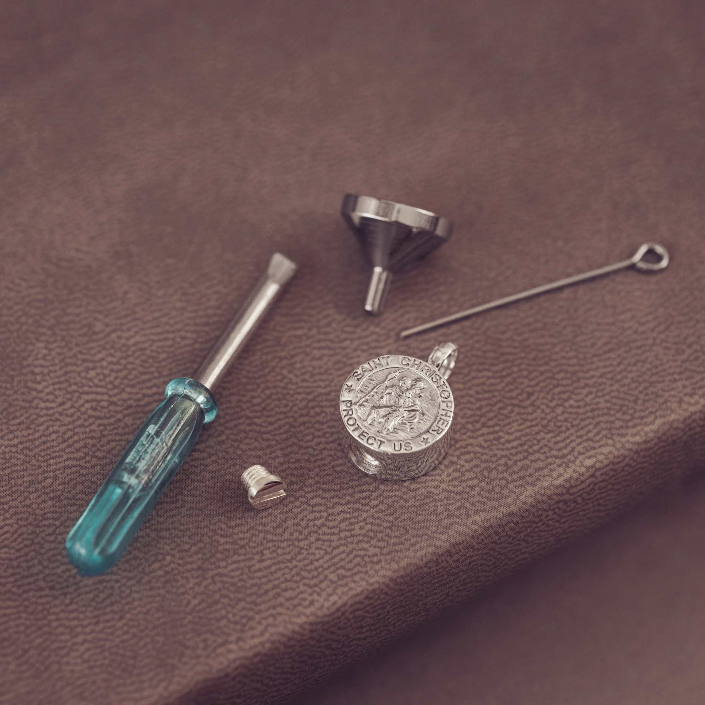 Silver pendant  on a leather surface, surrounded by tools like a screwdriver and funnel.