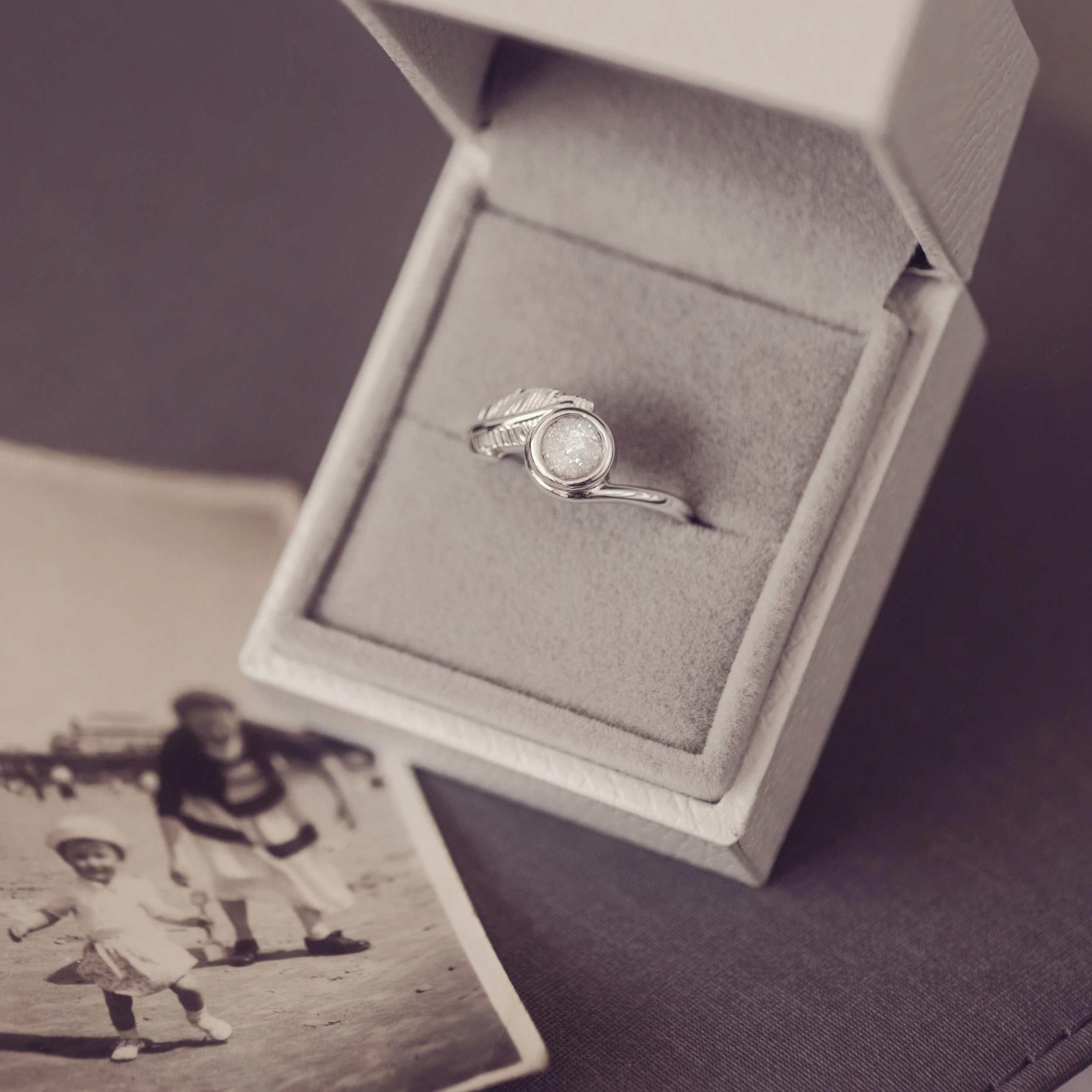 A silver ash filled feather ring in a jewellery box next to a black and white photograph