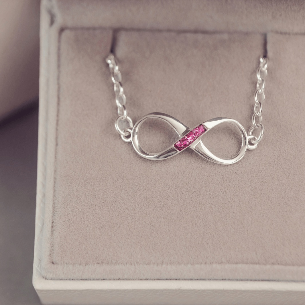 Silver infinity necklace with pink gemstones on a jewelry box