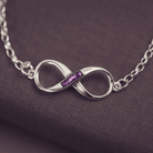 Silver infinity necklace with purple stones on a dark fabric background