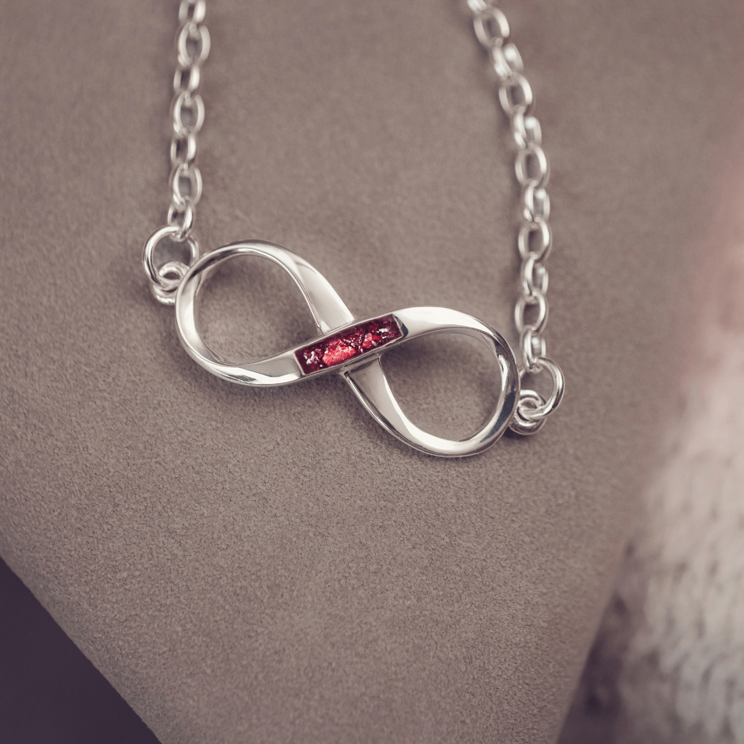 Silver infinity necklace with a red gemstone on a neutral background