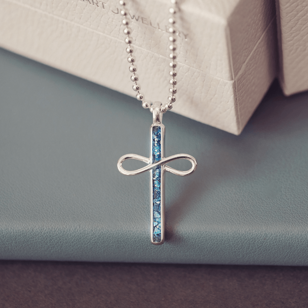 Silver cross necklace with blue stones on a light gray surface