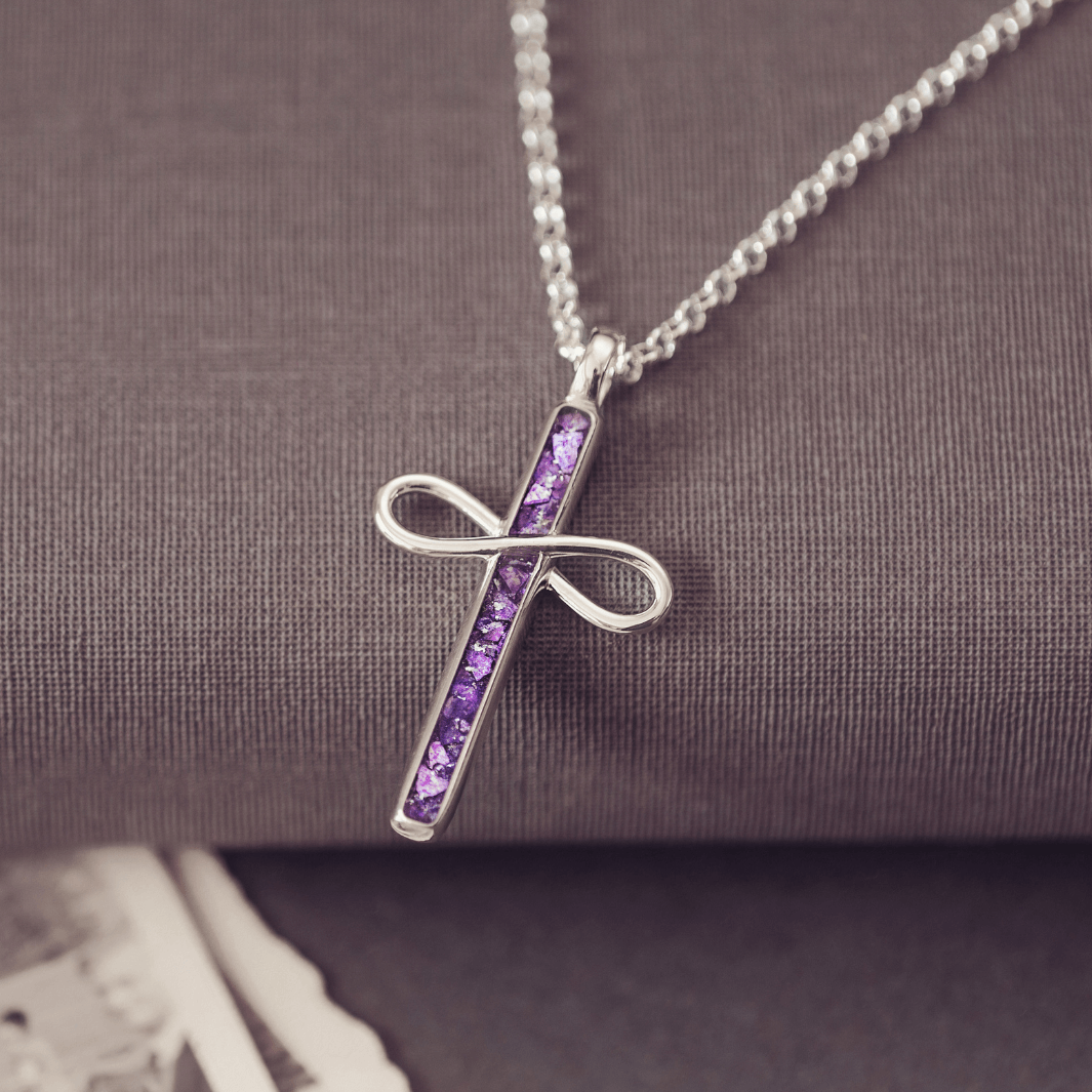Silver cross necklace with purple stones on a textured surface